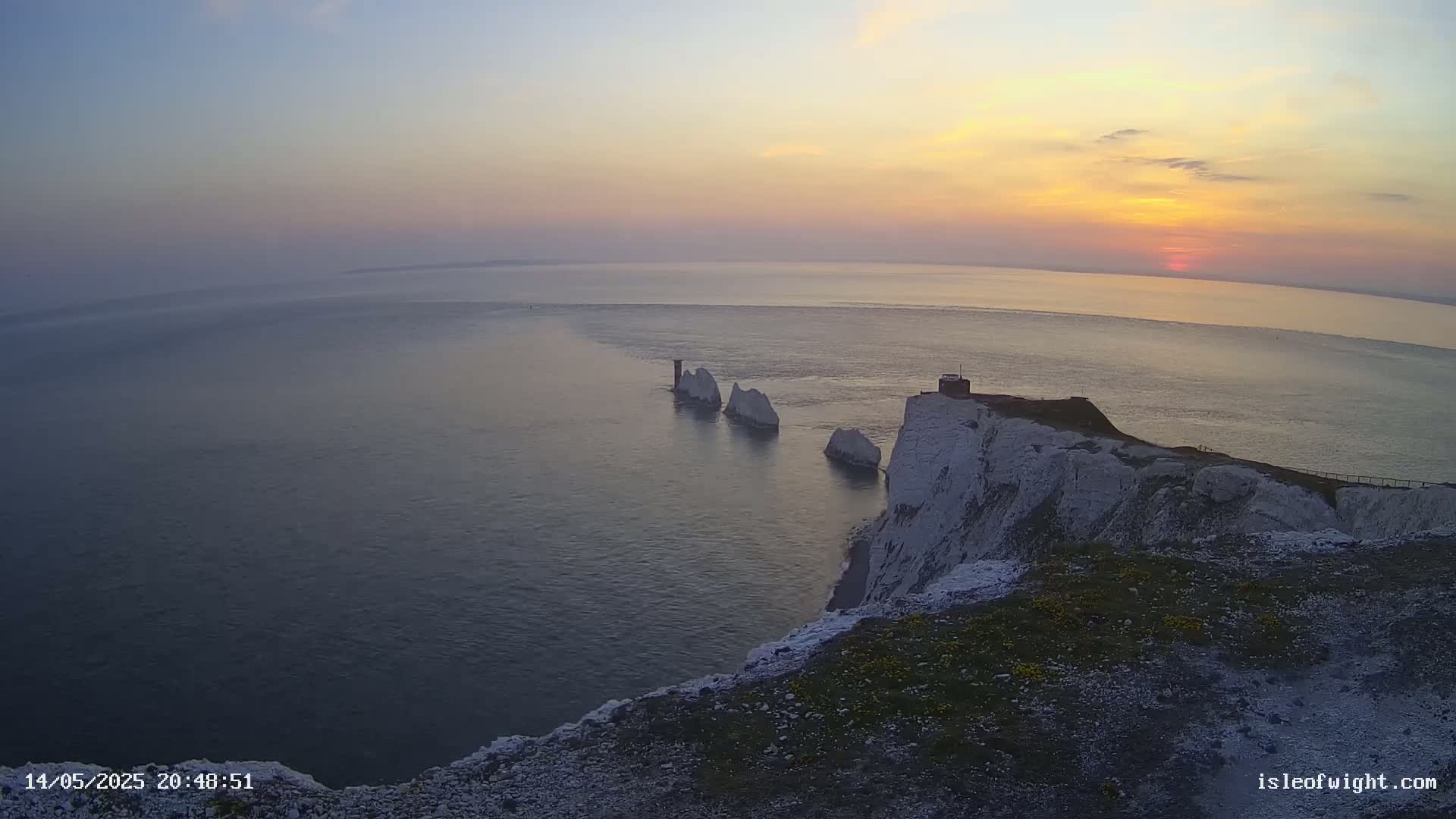 White cliffs overlook a calm sea at sunset, with several smaller white rock formations visible in the water.