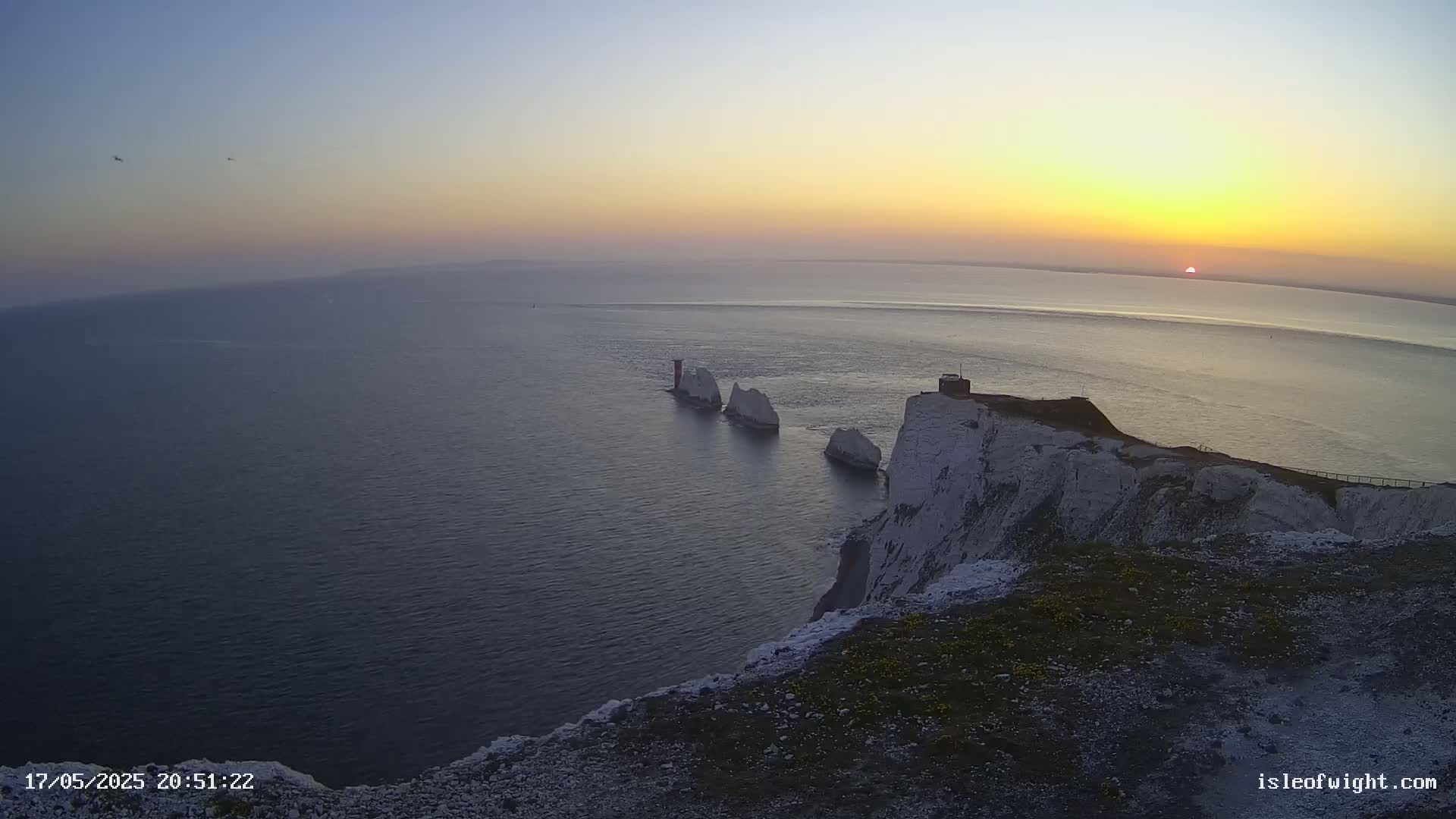 White cliffs overlook a calm sea at sunset, with several smaller white rock formations visible in the water.
