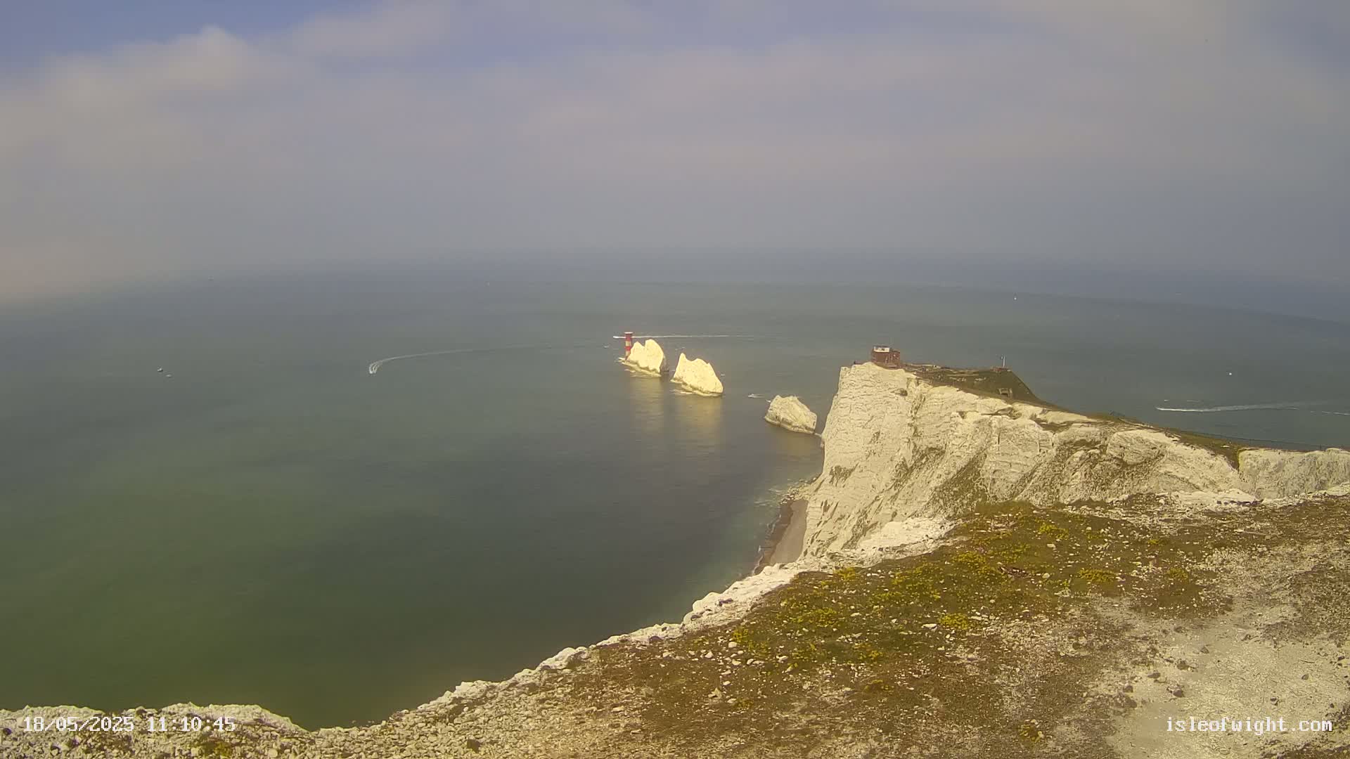 A hazy view shows white cliffs overlooking the sea, with two prominent rock formations and a small building visible in the distance.