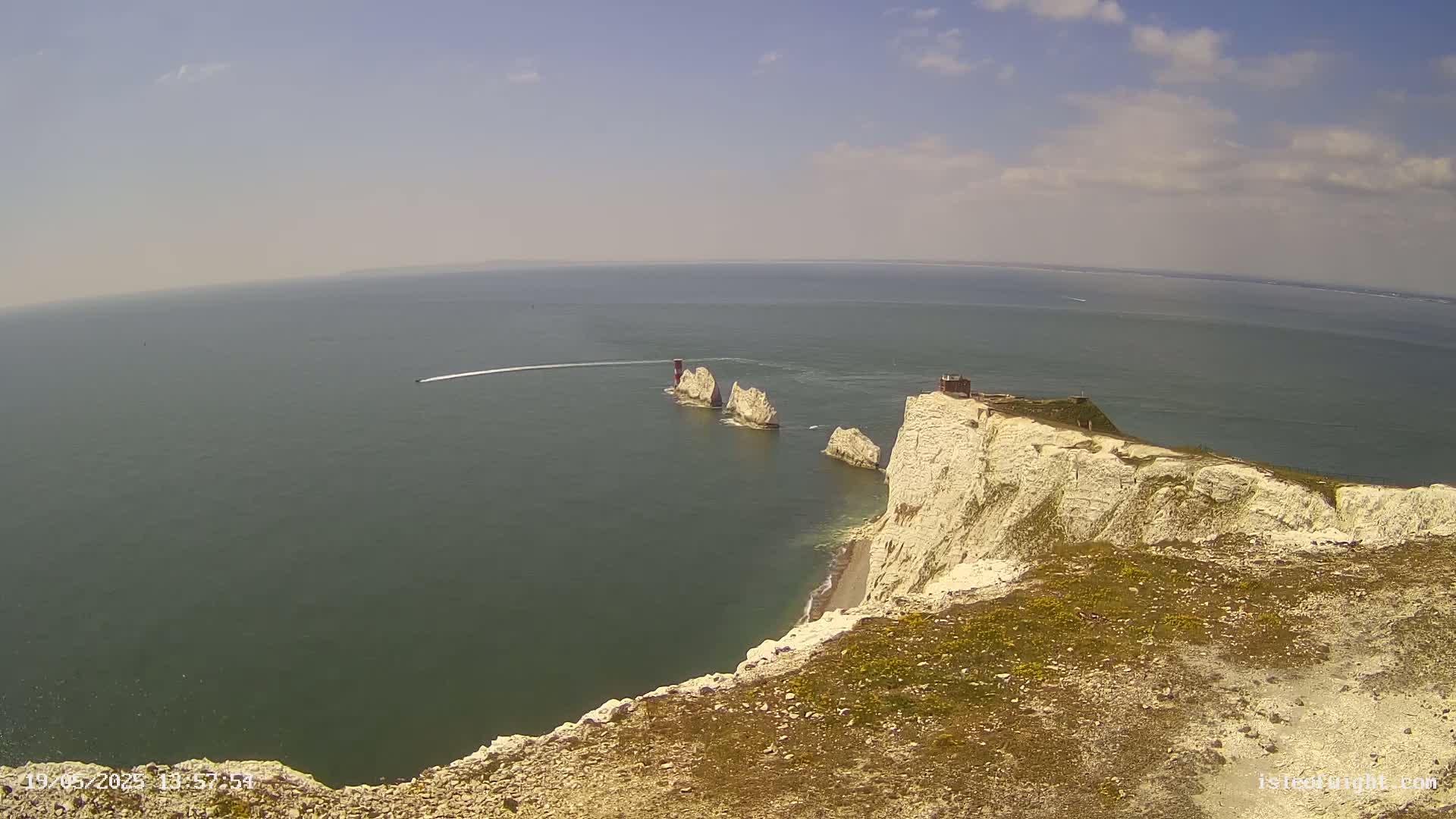 White cliffs overlooking a calm sea with a chain of small islands and a boat leaving a wake.