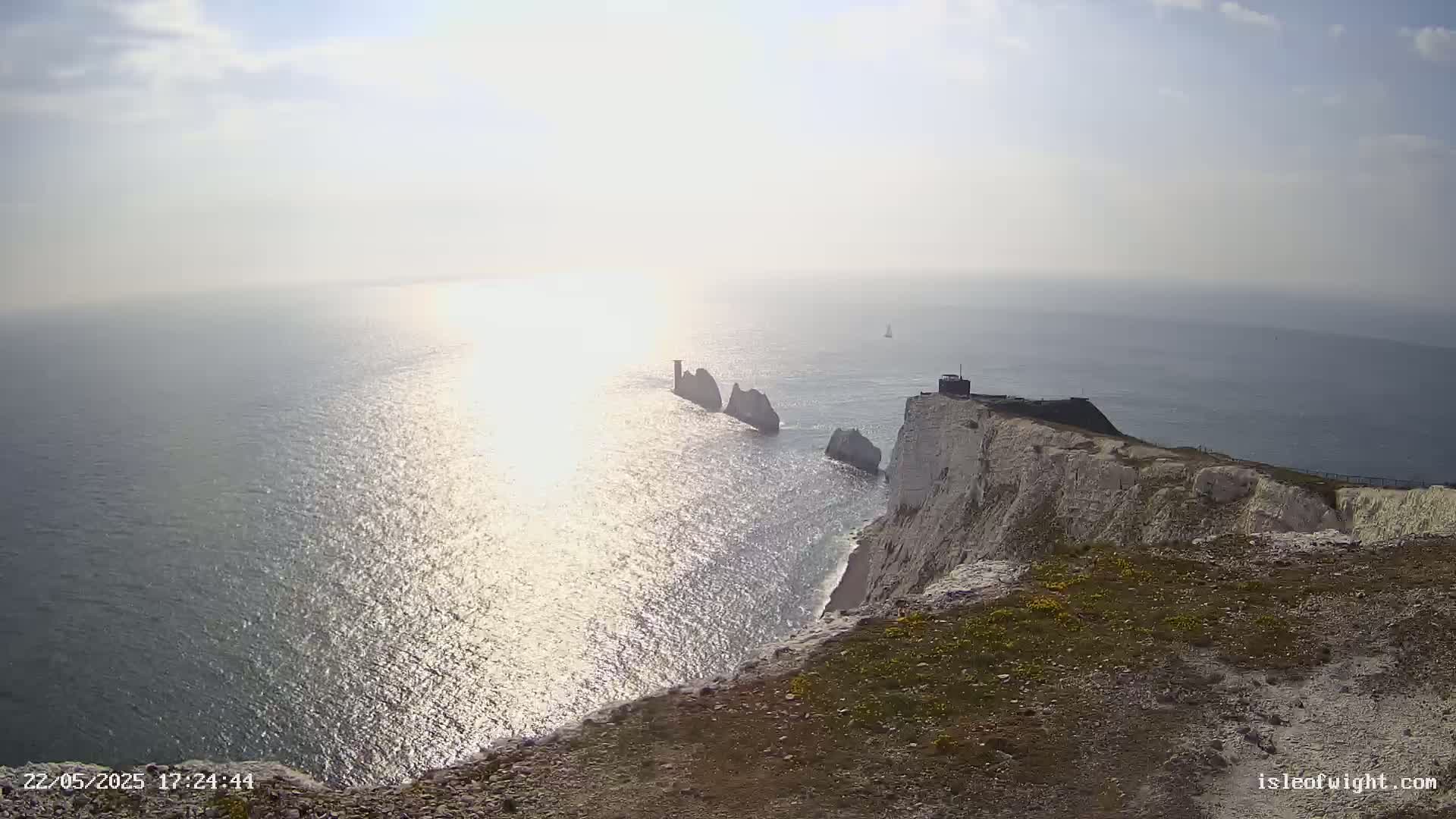 White cliffs overlooking a sunlit sea with several stacks of rock visible in the distance under a mostly sunny sky.