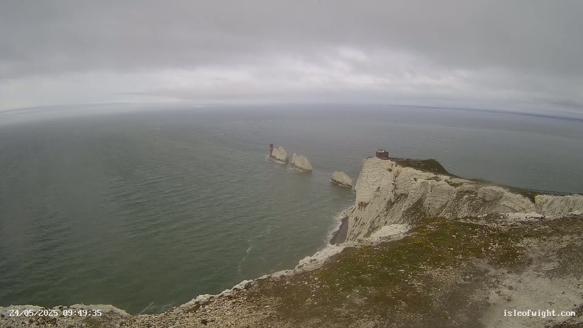 White cliffs overlooking a grey sea and three distant stacks under an overcast sky.