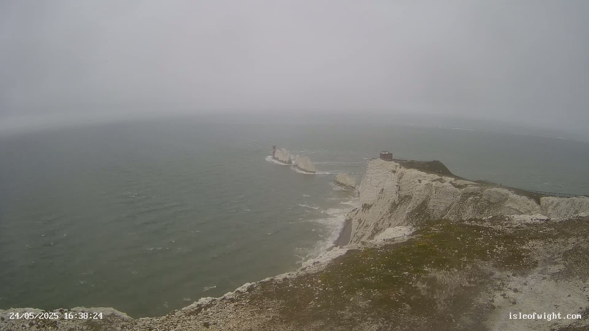 White cliffs overlook a foggy sea with a chain of rocky islands visible in the distance.