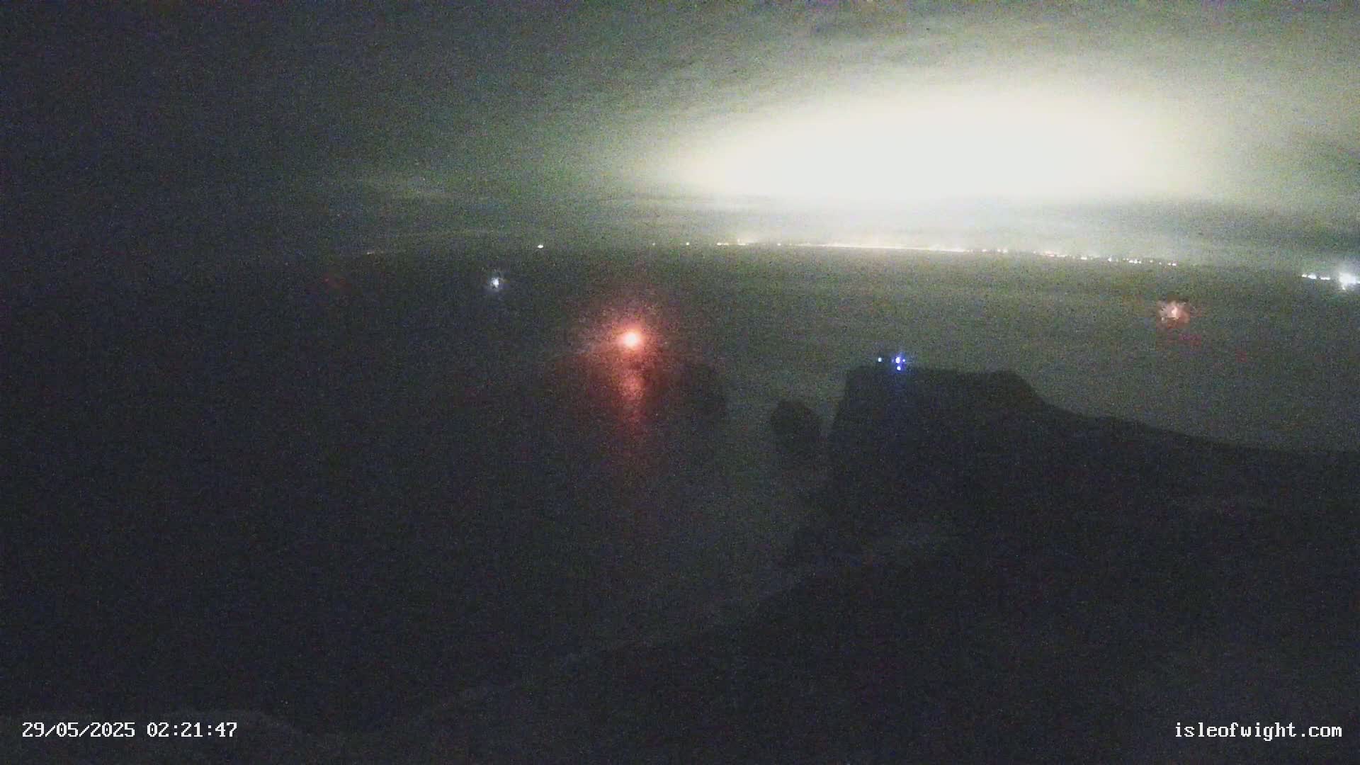 A nighttime, hazy view of a body of water with distant lights on the horizon and a few faint lights closer to the foreground.