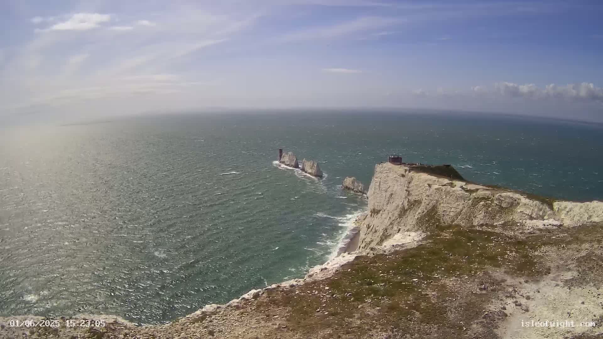 A windy, sunny day reveals white cliffs overlooking a choppy sea with a group of distant, smaller rock formations.