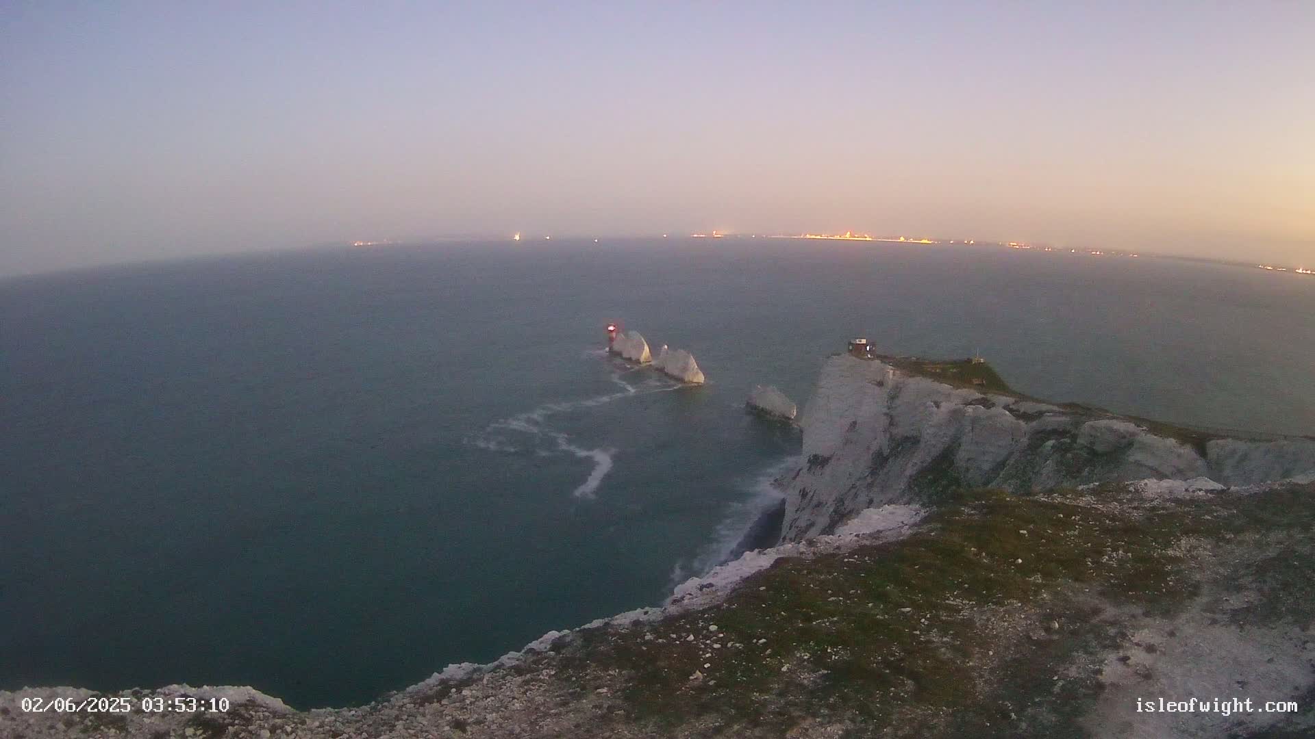 White cliffs overlook dark blue water, where three white rock formations stand out, under a dusky sky.