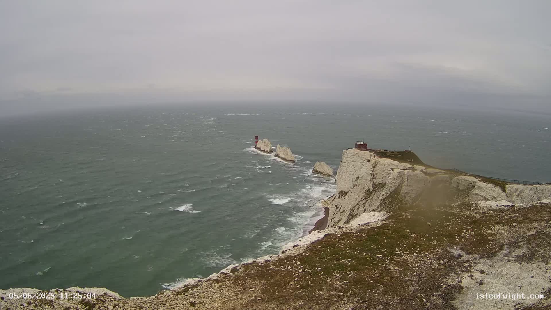 White cliffs meet a choppy, gray sea under an overcast sky, with a small island and lighthouse visible in the distance.