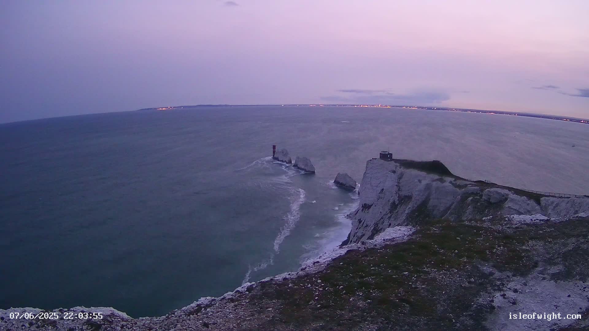 White cliffs overlook a calm, twilight sea with a small island and lighthouse visible in the distance.