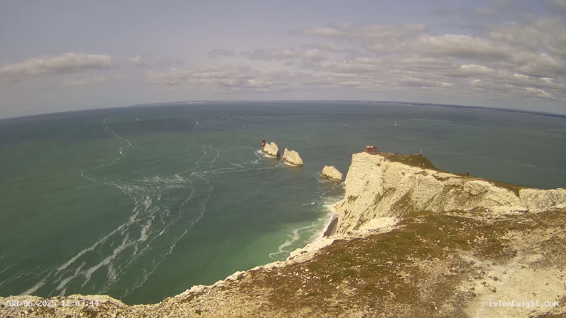 White cliffs overlooking a green sea with several small, distant islands and a partly cloudy sky.