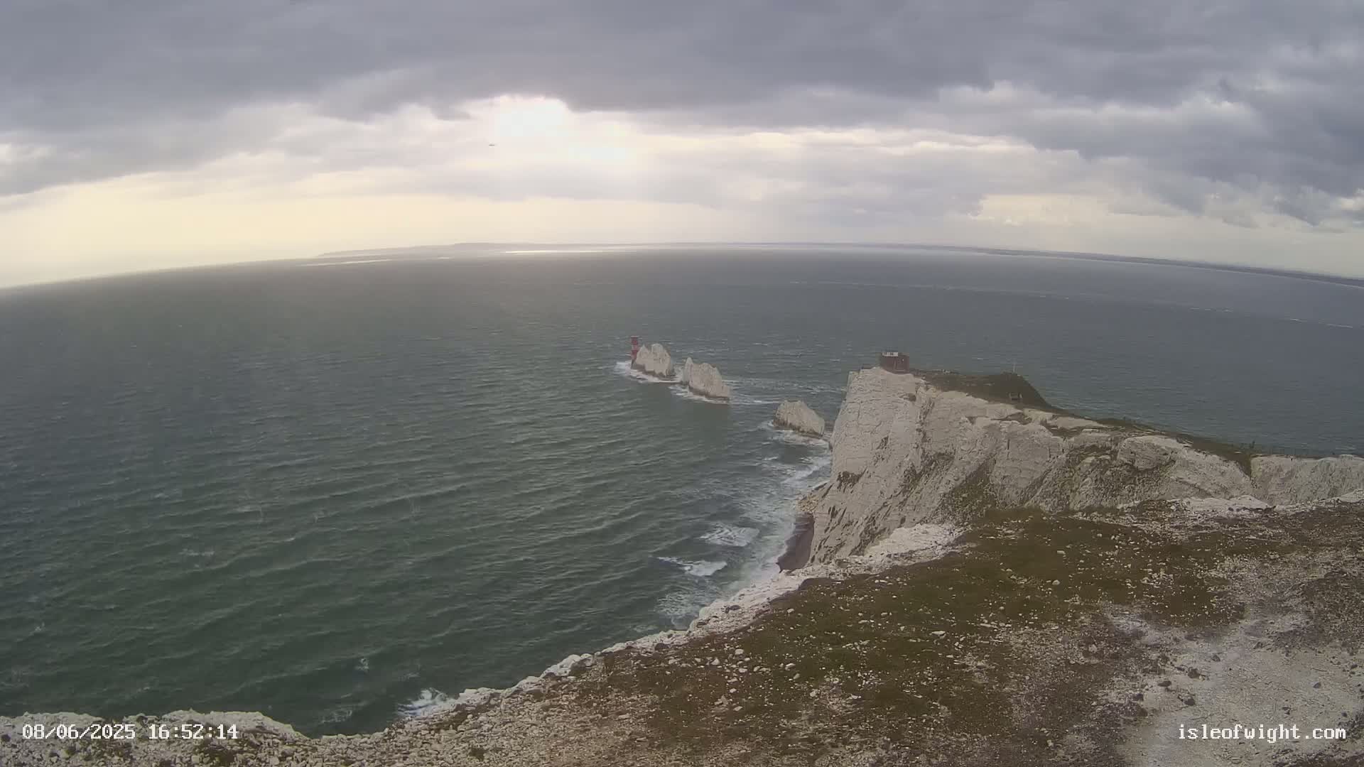 White cliffs meet a choppy sea under a cloudy sky, with several white rock formations visible in the water.