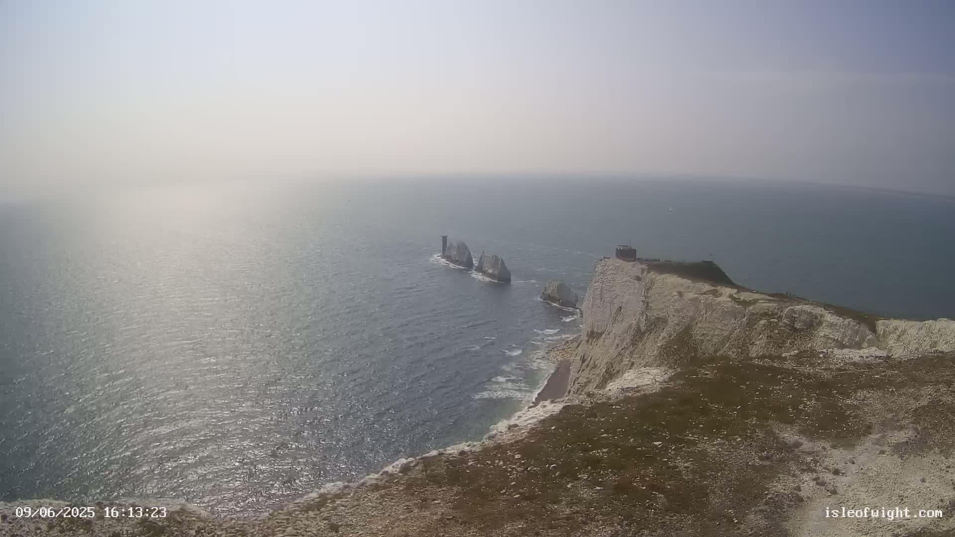 A hazy, sunny day reveals a coastal scene with white cliffs overlooking the ocean and several white rock formations in the water.