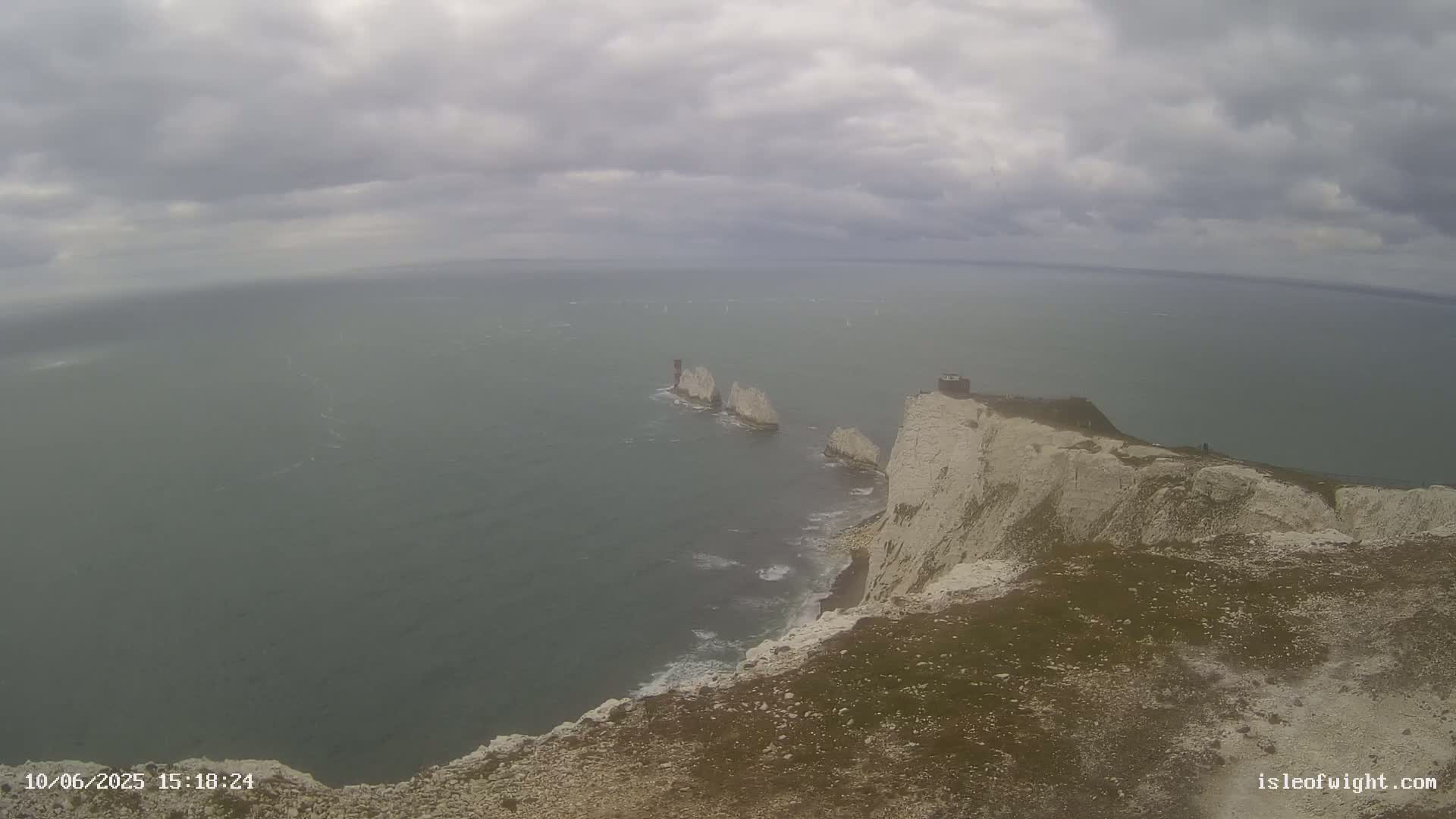 White cliffs meet a gray, overcast sea where several small, white rock formations rise from the water.