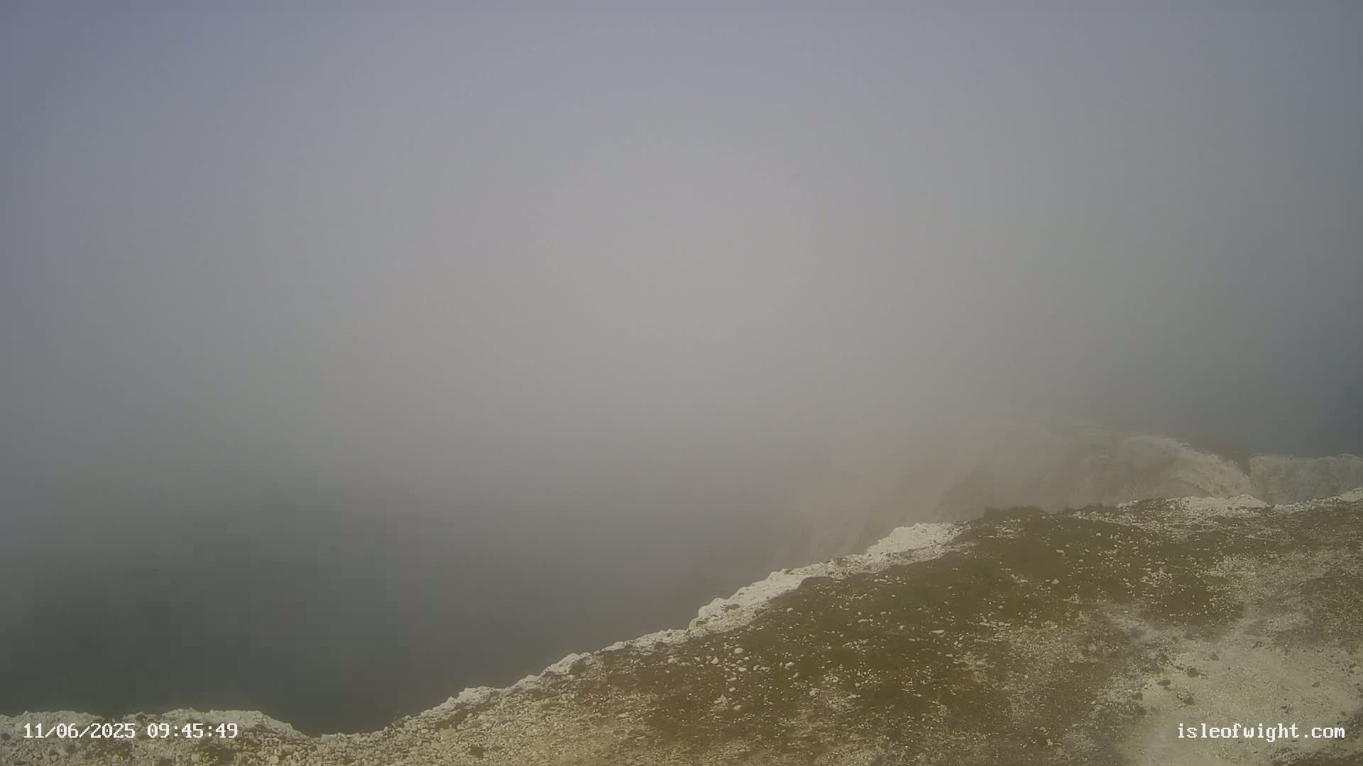 A foggy, overcast view of a rocky cliff edge overlooking a body of water.