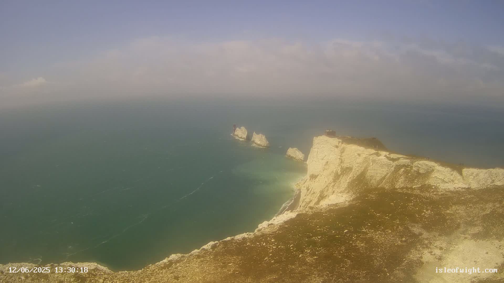 A hazy view shows white cliffs overlooking a green sea, with several smaller white rock formations visible in the water.
