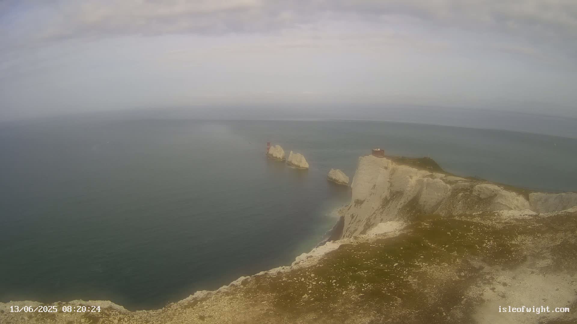 A hazy view shows a rocky coastline with a small structure on a cliff overlooking several white rock formations in the sea.
