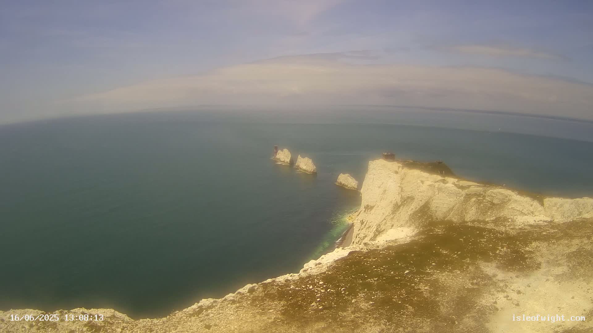 White cliffs overlook a hazy, teal sea where several small, white rock formations are visible in the distance.
