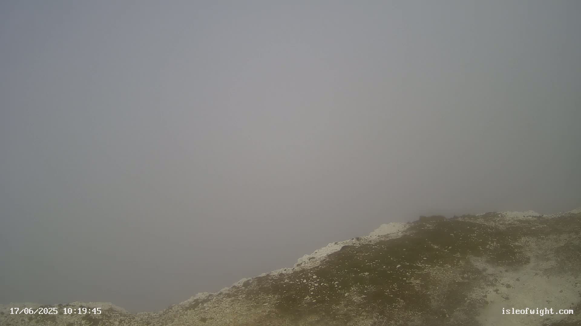 A rocky, sparsely vegetated landscape is shrouded in thick fog.