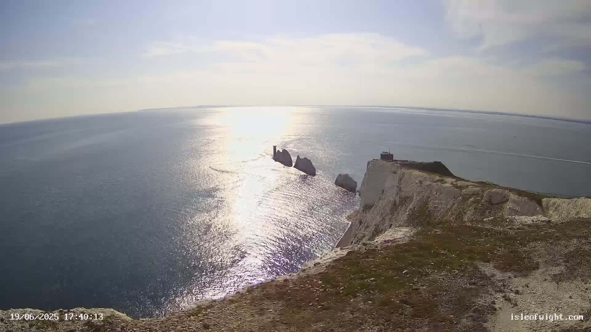 A sunny day reveals a high-angle view of white cliffs overlooking a calm sea with several stacks visible in the distance.