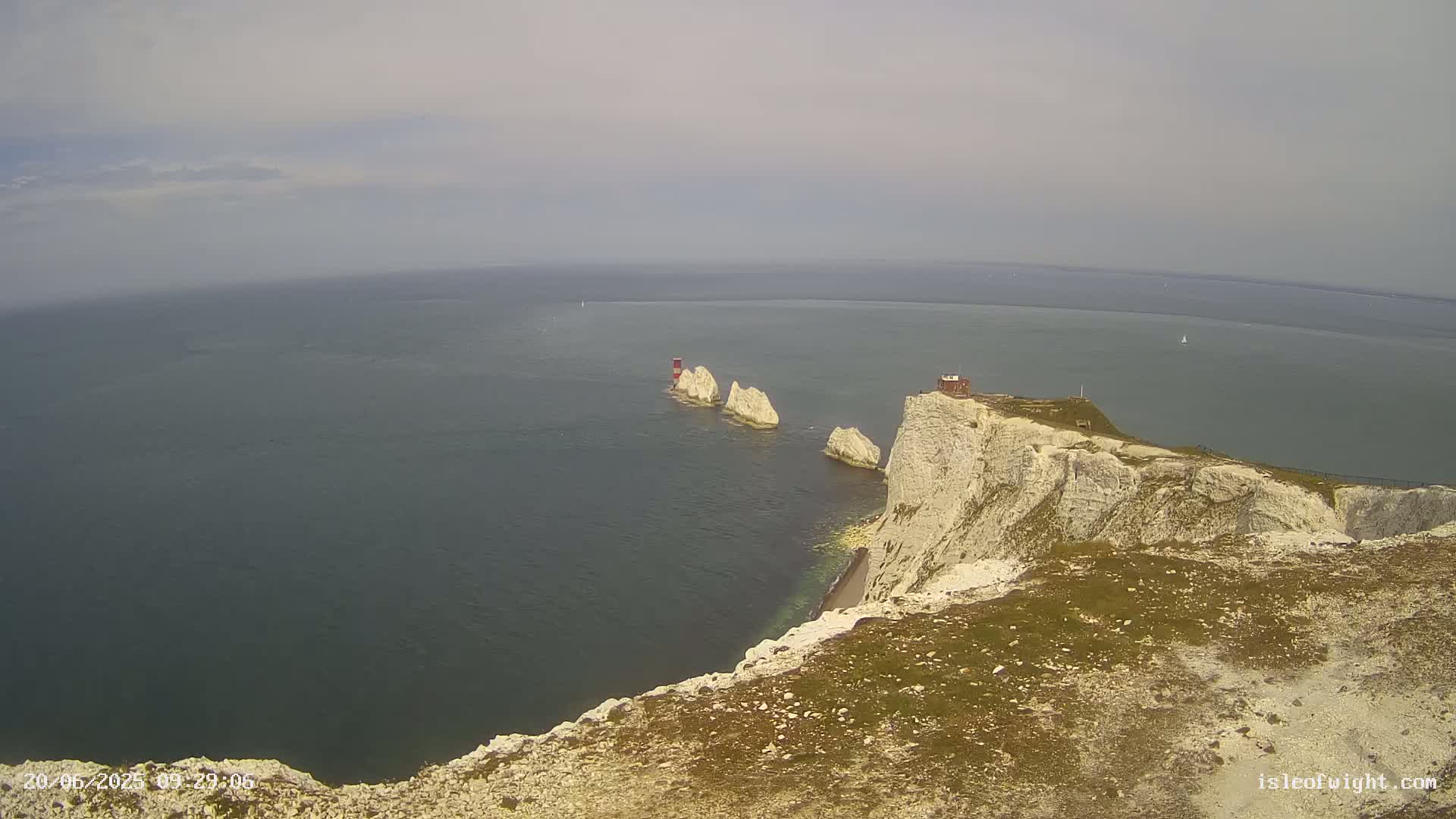 White cliffs overlook a calm sea with several small, distant islands and a small building atop one of the cliffs.