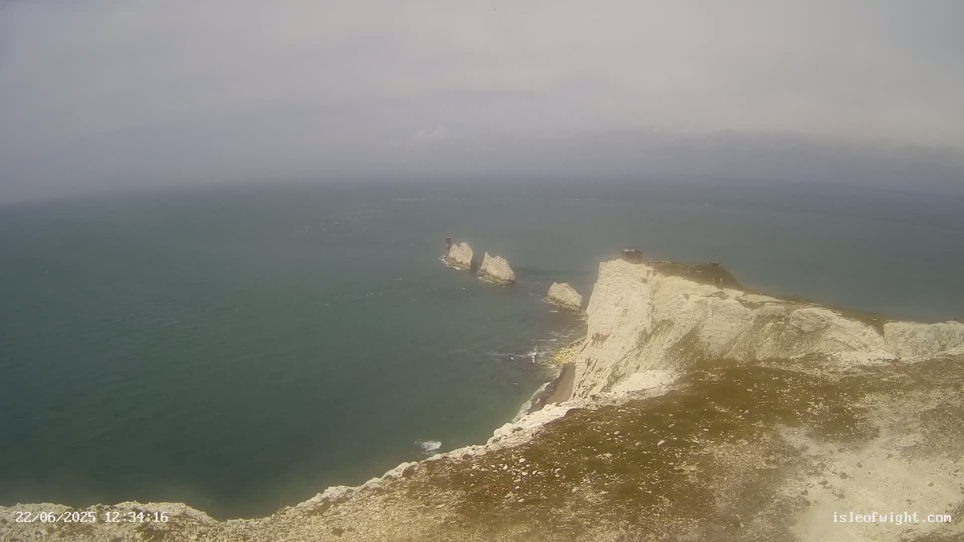 White cliffs meet a hazy, grey sea, with several smaller rock formations visible in the water.