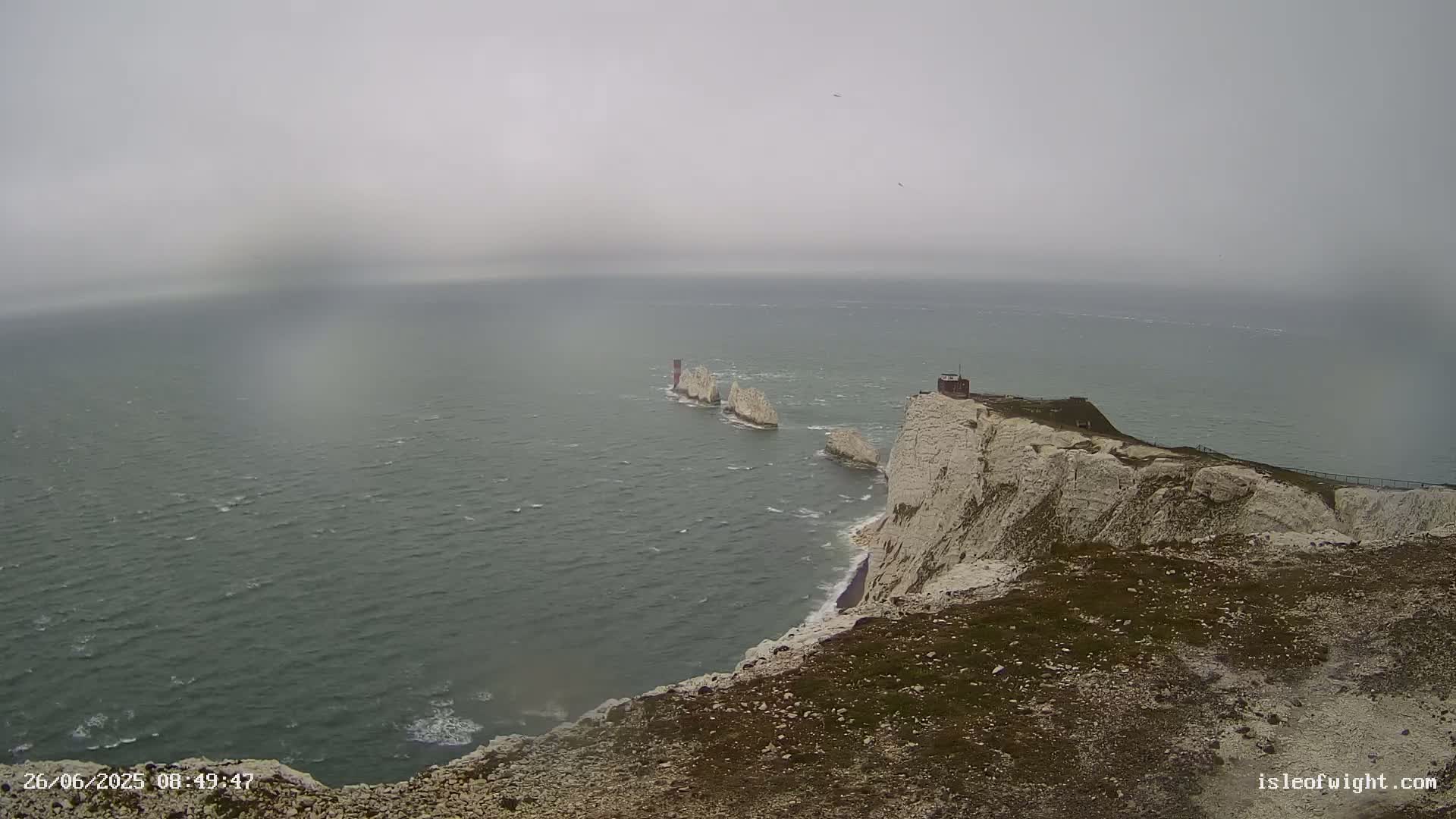 White cliffs overlook a choppy sea with a line of distant rock formations under an overcast sky.