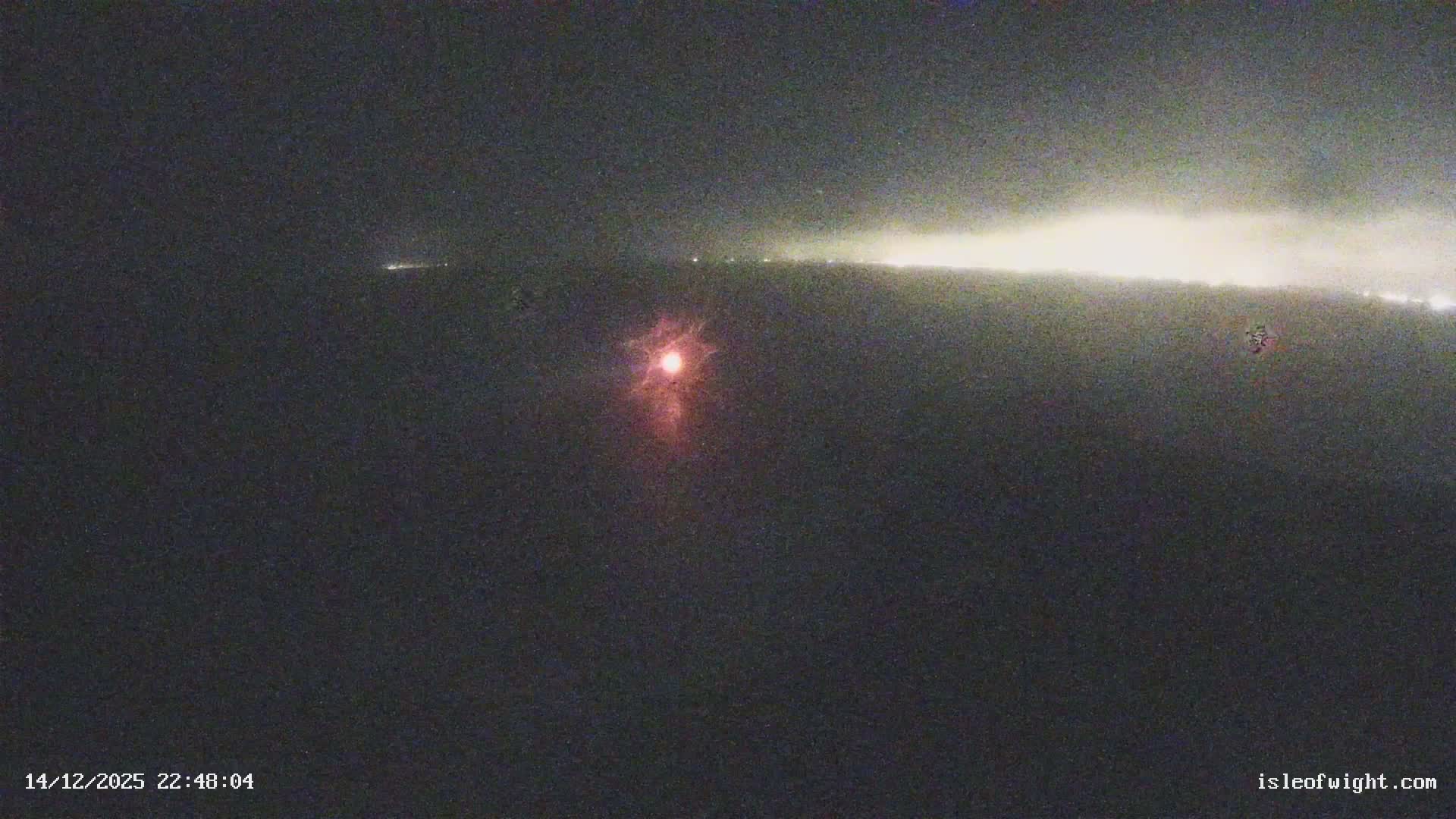 An expansive view captures the iconic Needles sea stacks and lighthouse off the Isle of Wight's white cliffs, with rough waves breaking against the shore under a mostly cloudy sky.