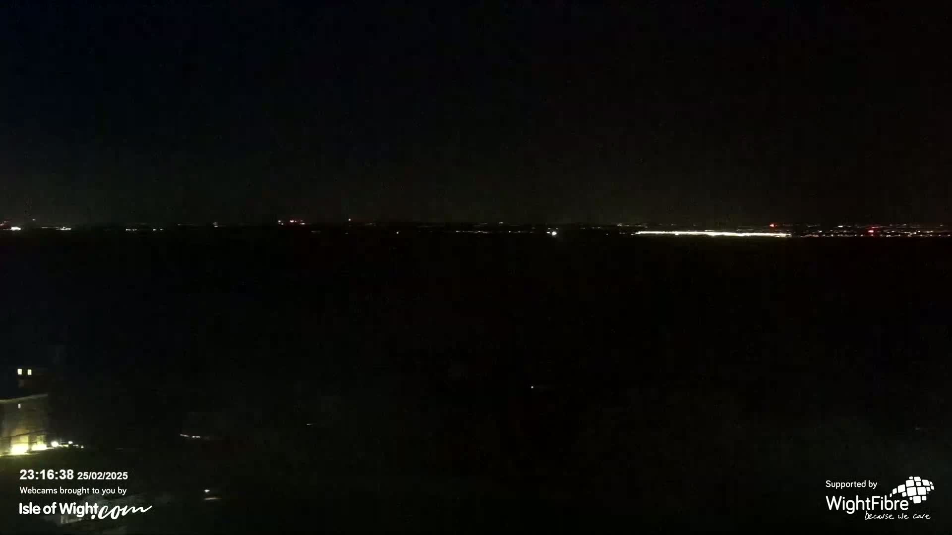 A nighttime view of a distant city skyline illuminated by lights under a clear, dark sky.