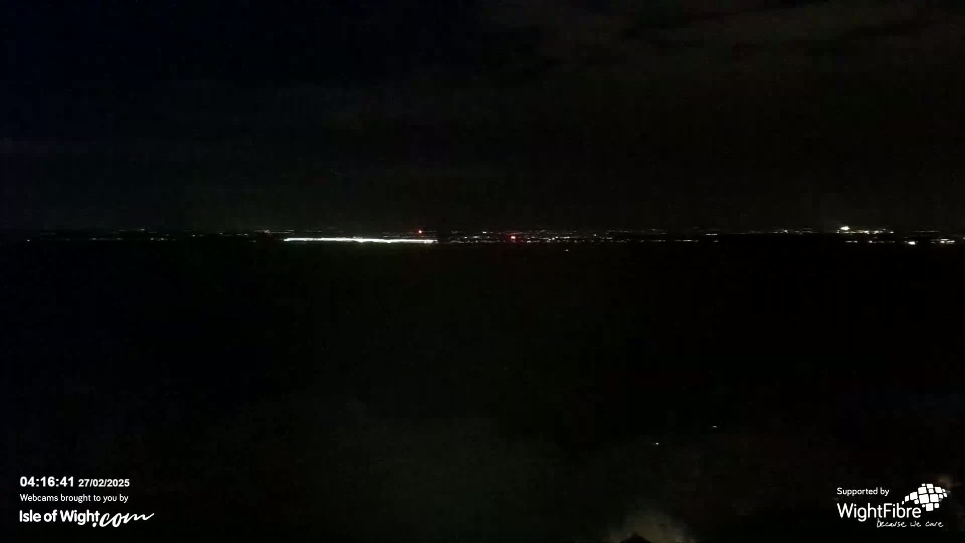A nighttime long shot shows a distant city skyline illuminated against a dark sky.