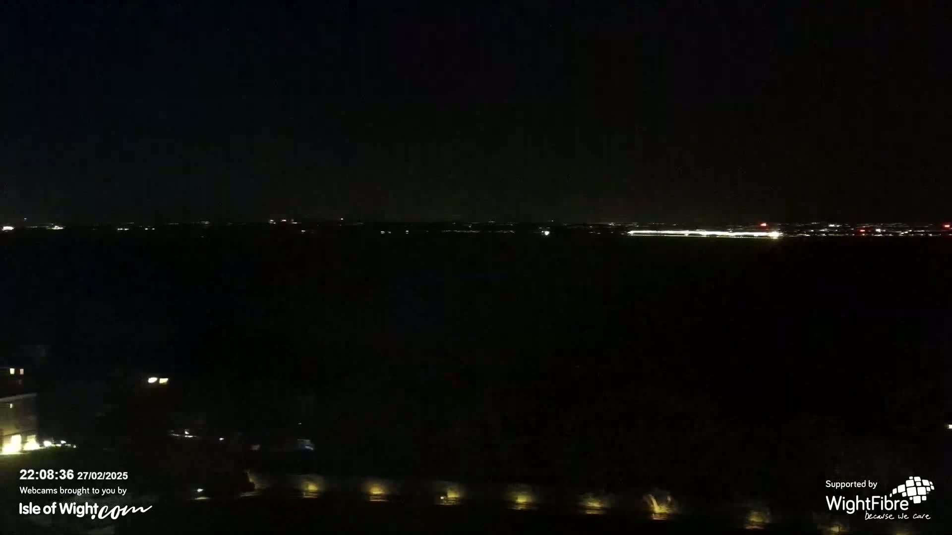A nighttime, dark view of a body of water with a distant, faintly lit city skyline.