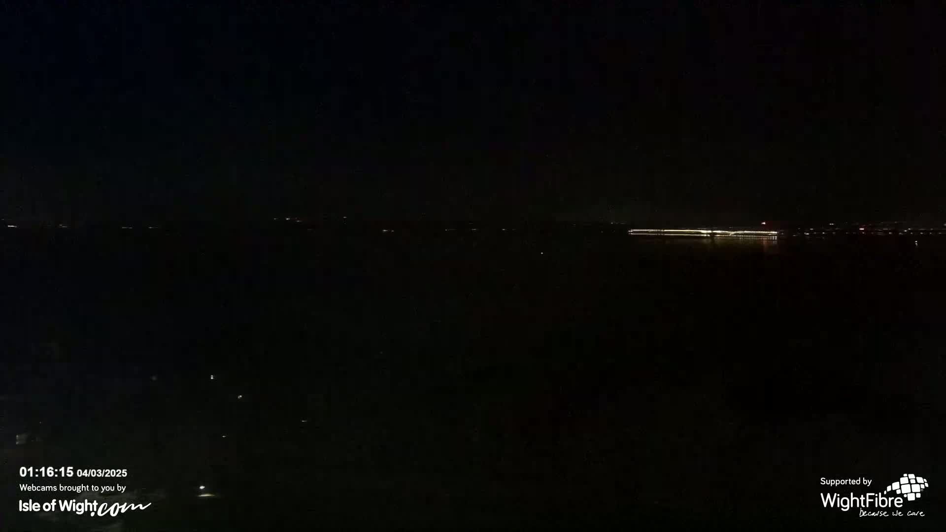 A dark, nighttime view of a body of water with a faintly illuminated distant shoreline.