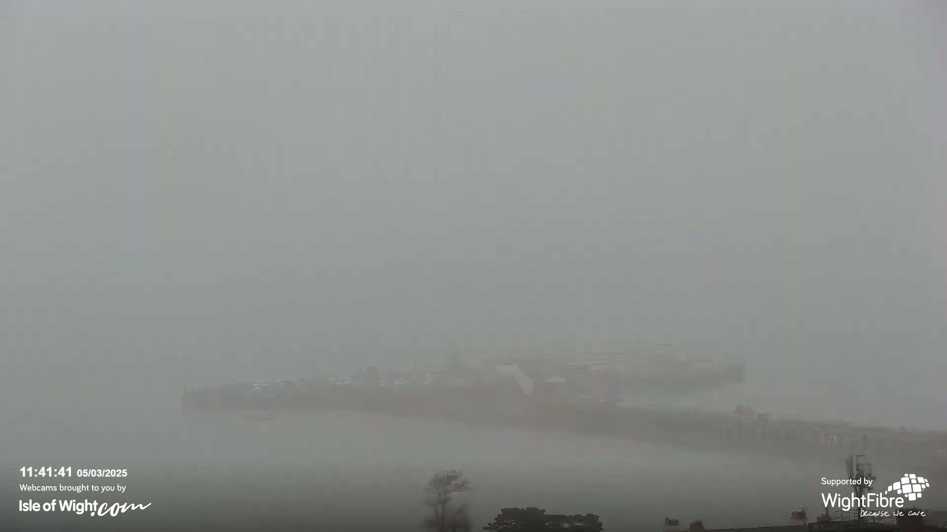 A thick fog obscures the view of a large vessel and some structures near the water.