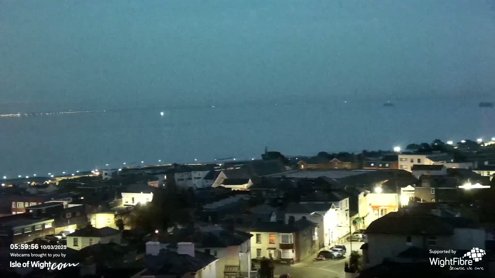 A nighttime view of a town situated near a body of water under a hazy, dark sky.