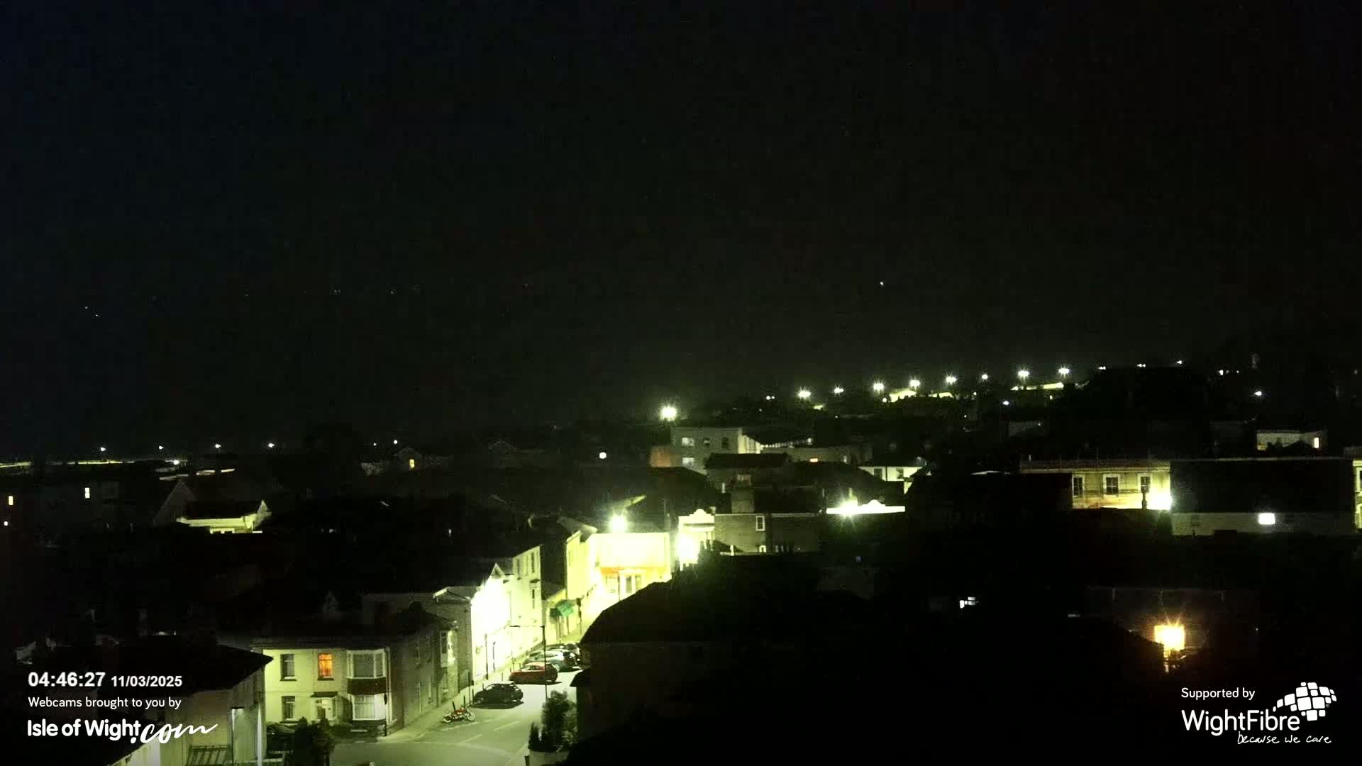 A nighttime view of a town with dimly lit buildings under a dark, clear sky.