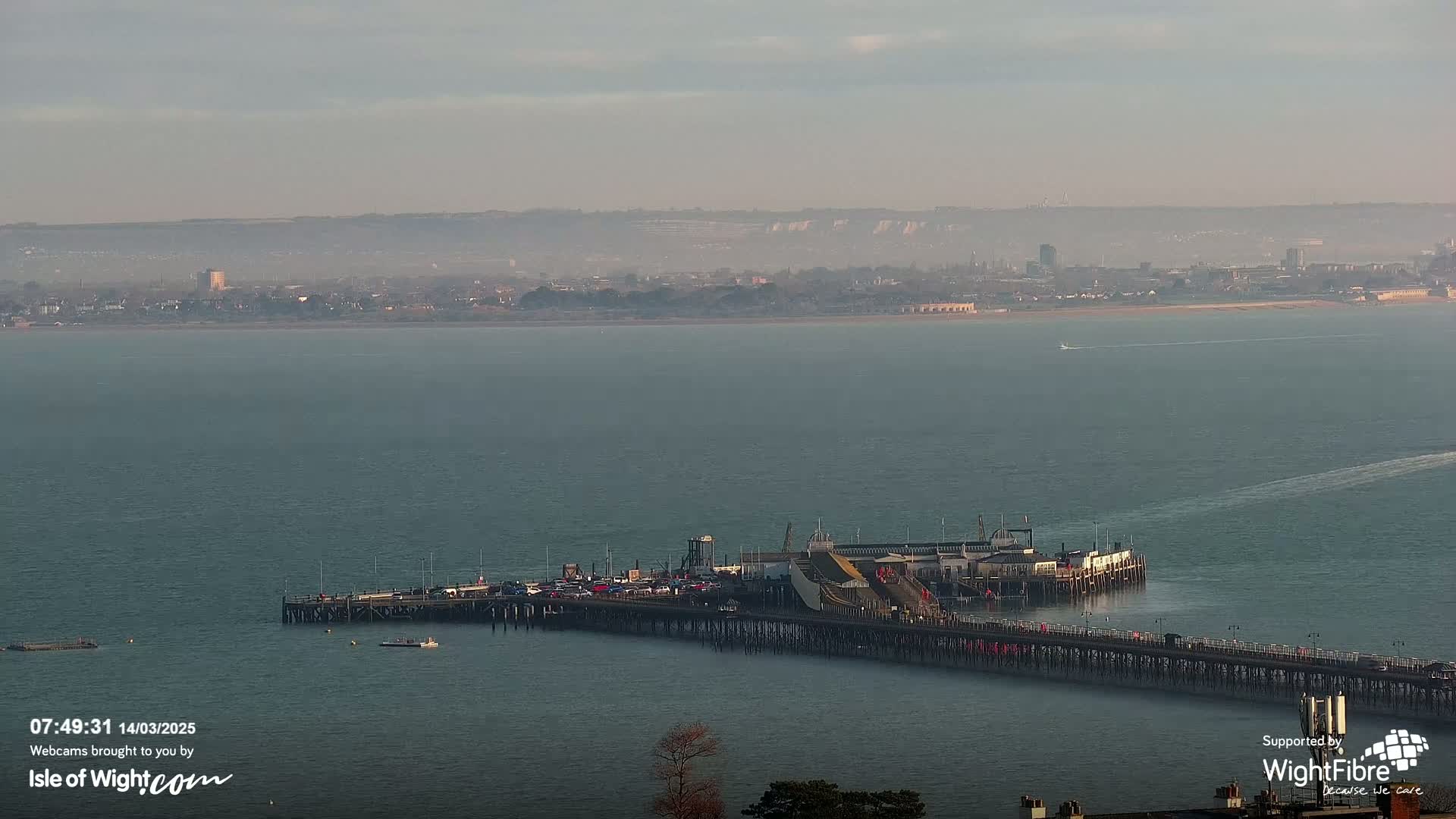 A long pier extends into a calm, hazy body of water, with a distant town visible under a muted sky.