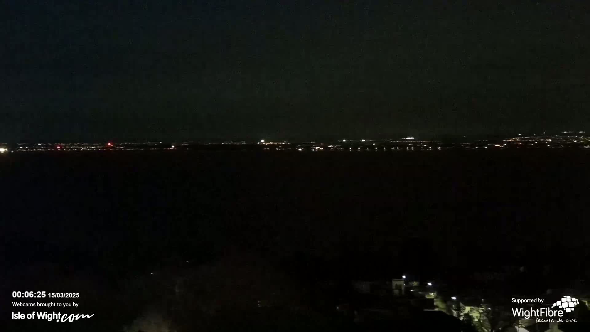 A nighttime view of a distant city skyline illuminated by faint lights, under a dark sky.