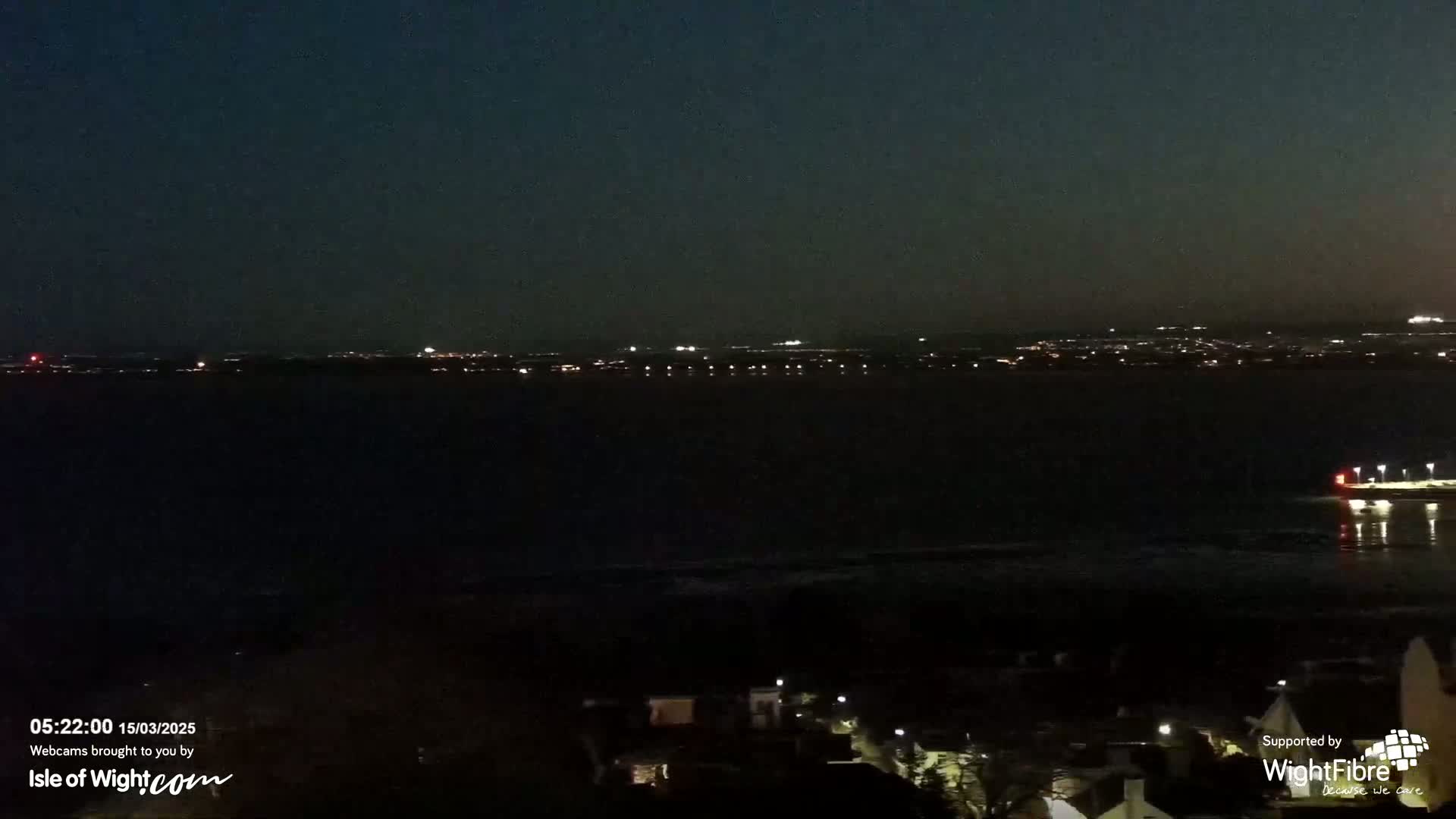 A nighttime view of a dark body of water with a distant, faintly lit cityscape under a clear, dark sky.