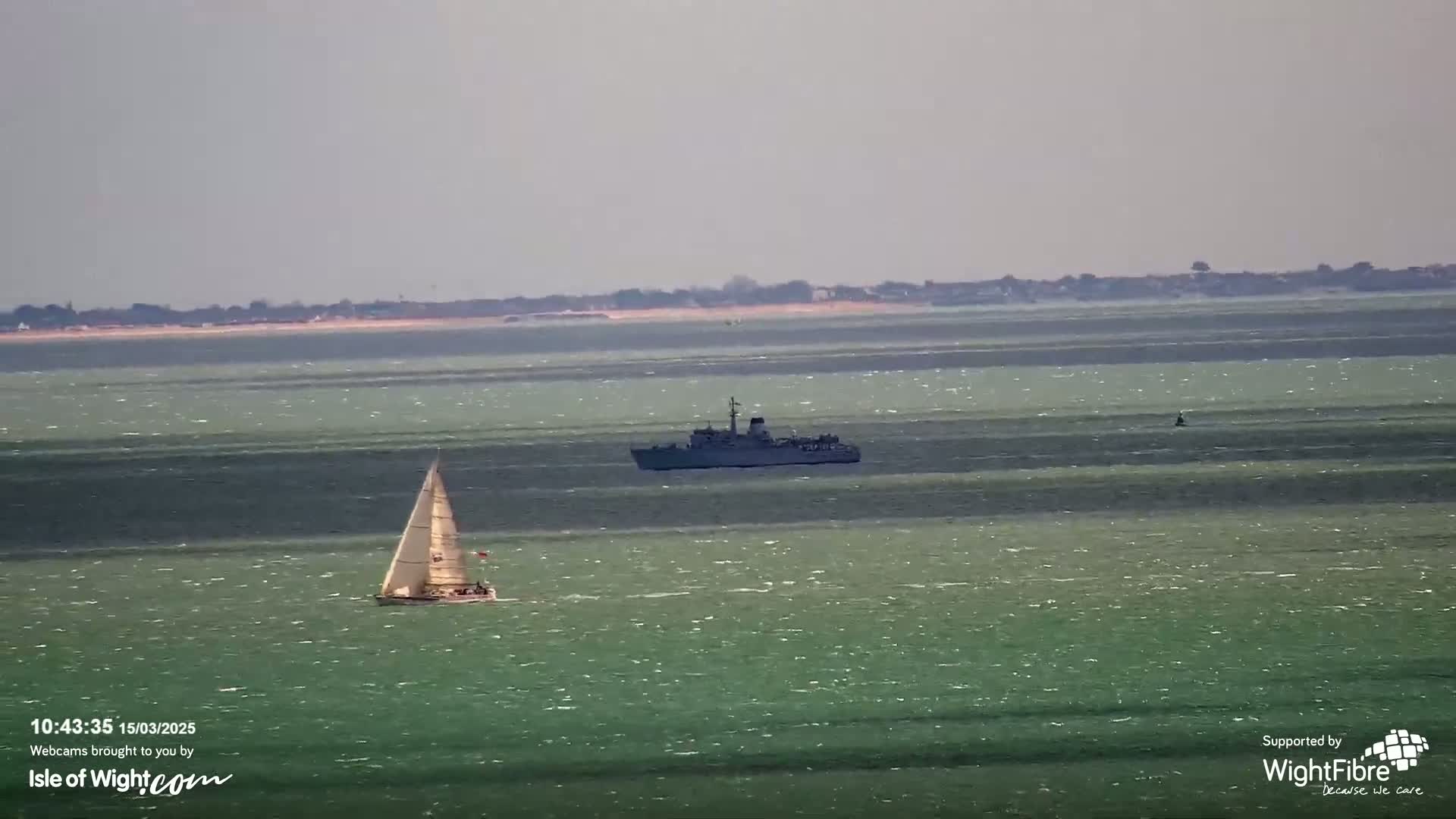 A sailboat and a warship are visible on a calm, greenish-blue sea with a distant landmass on the horizon.