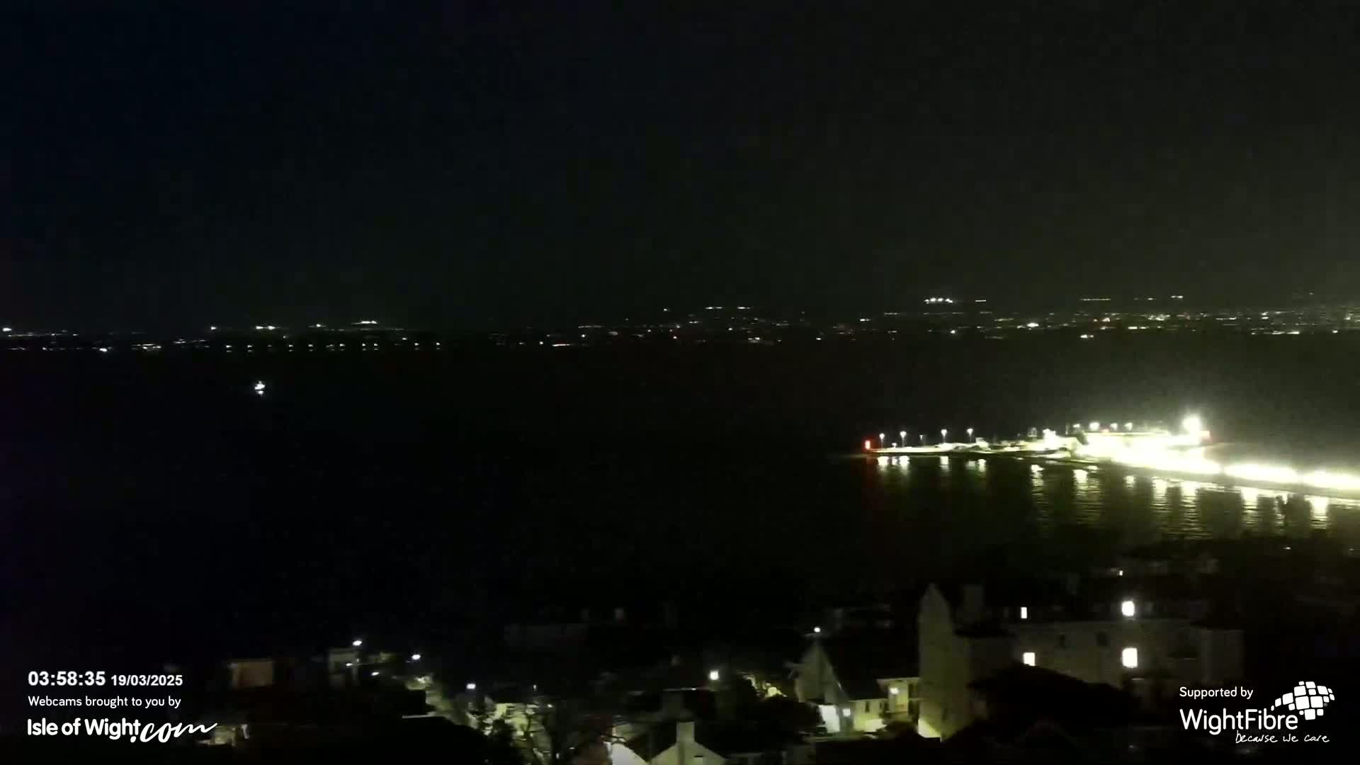A nighttime view of a body of water with a city skyline in the distance and illuminated buildings along the shore closer to the viewer.