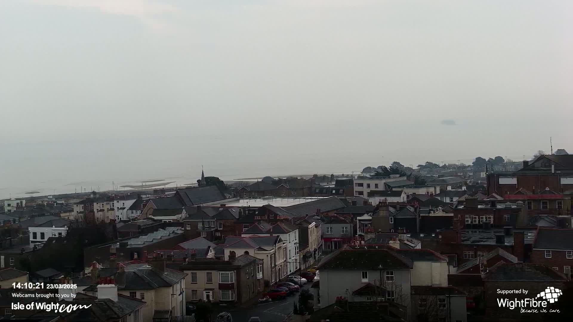 A foggy overcast day reveals a coastal town's rooftops extending to a hazy sea.