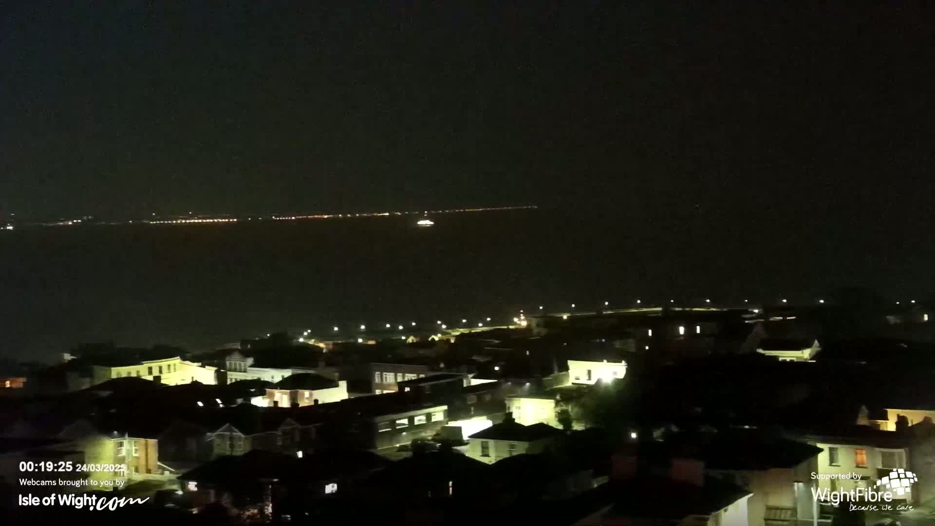 A nighttime view of a town's lights near a dark body of water with a distant line of lights on the far shore.