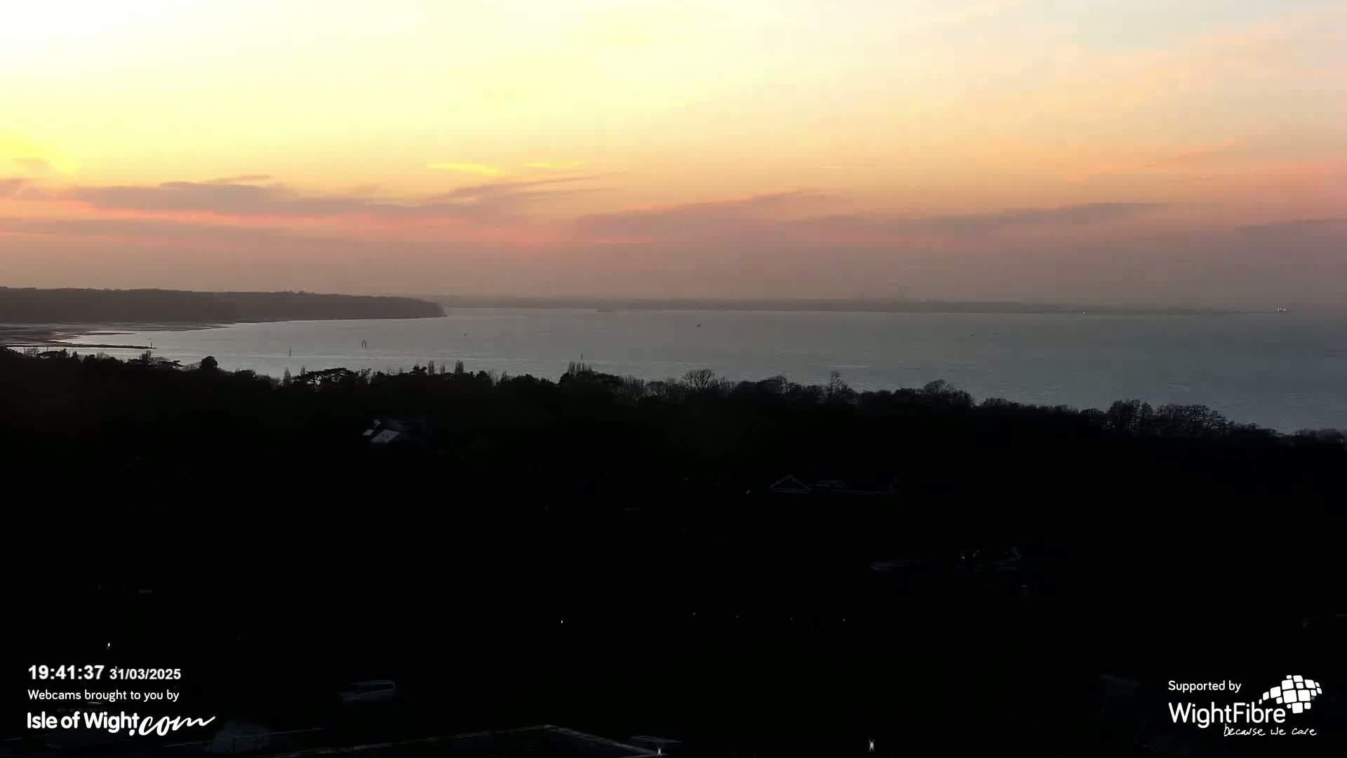 A tranquil sunset over a calm body of water, viewed from a wooded hilltop.