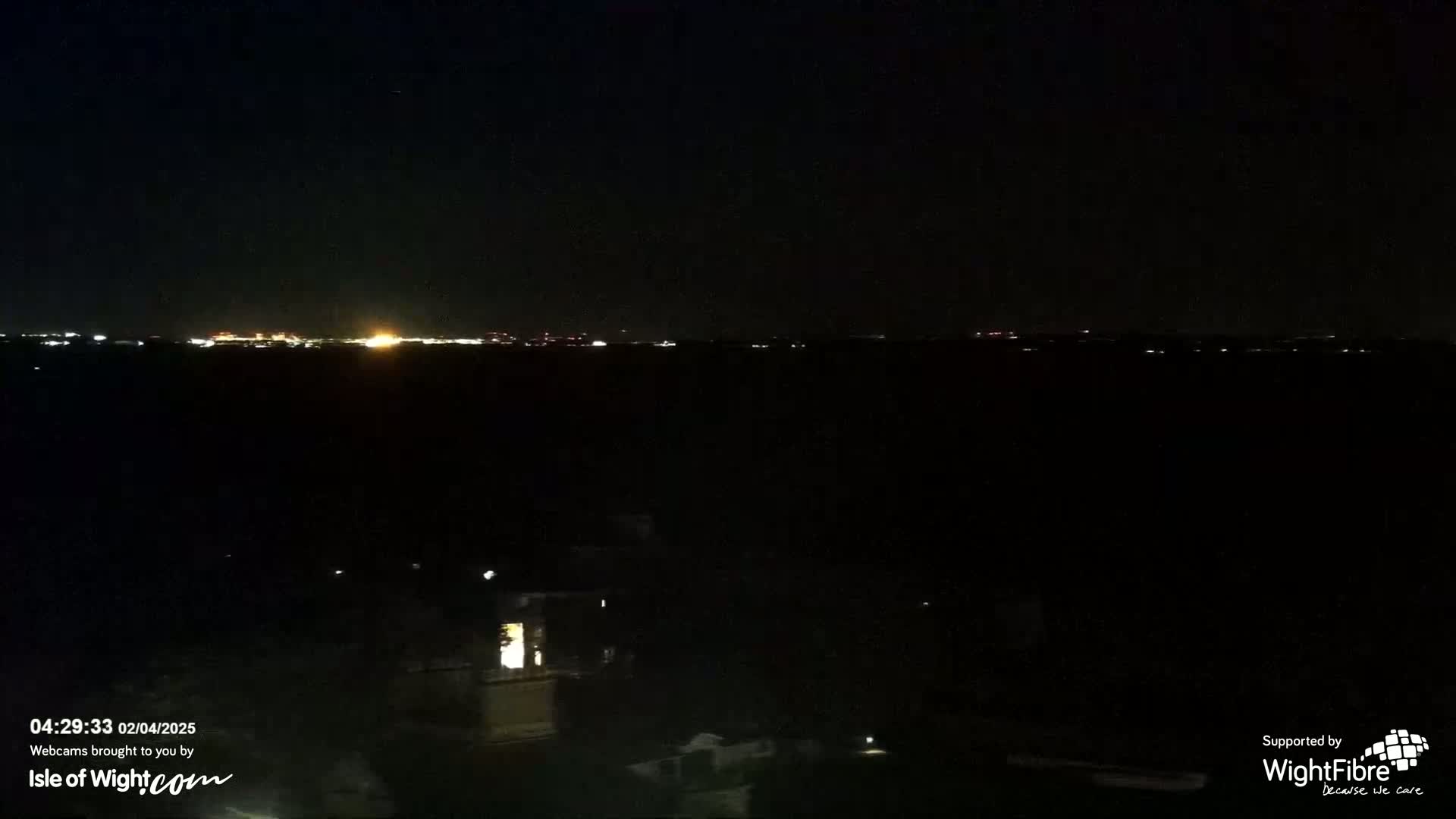 A nighttime view of a distant city skyline illuminated by lights, across a dark body of water.