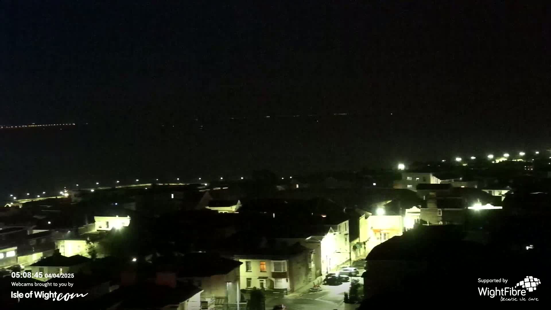 A nighttime view of a coastal town with dimly lit houses and a dark sea in the background.