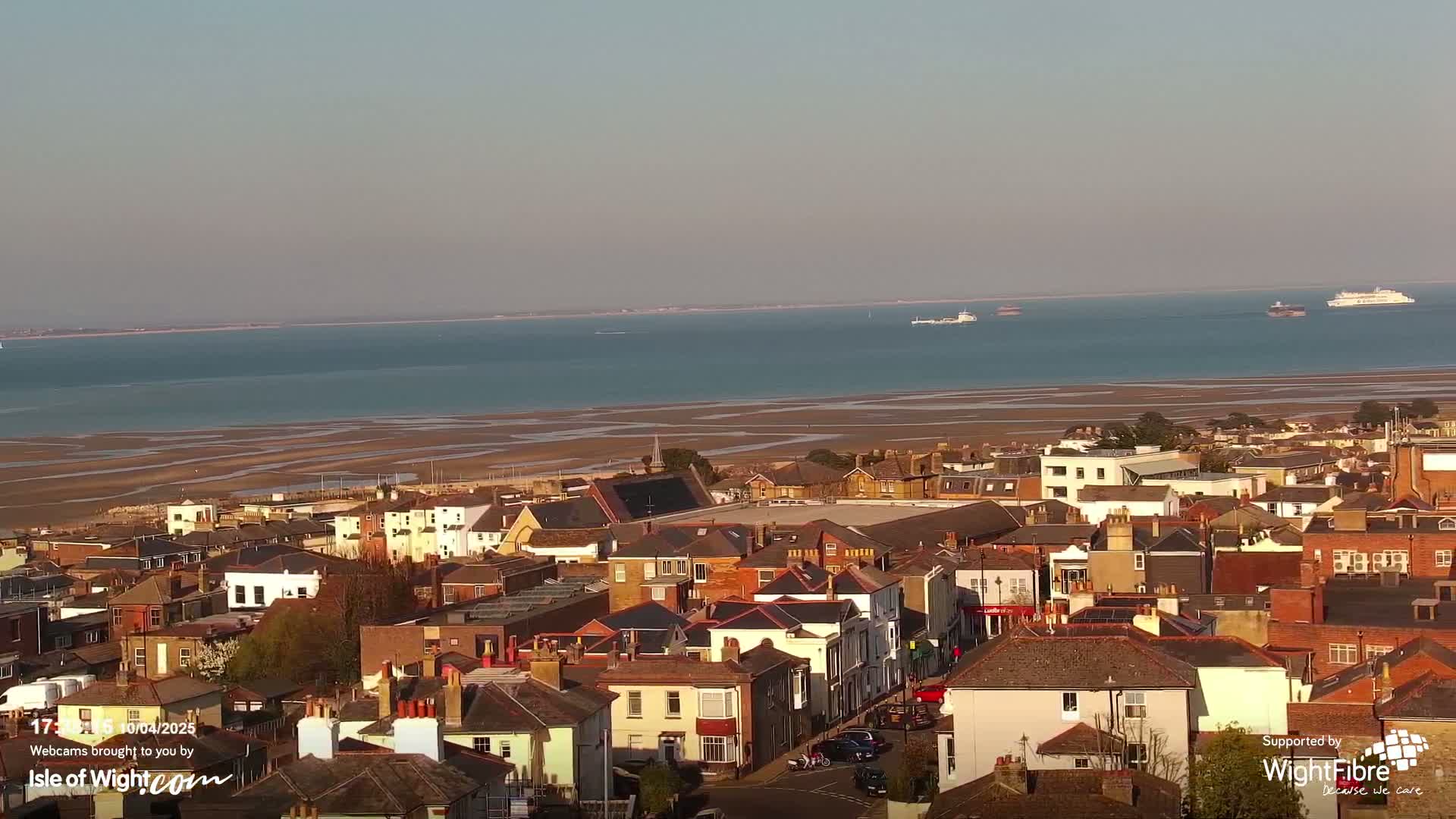 A coastal town with many houses and buildings overlooks a wide expanse of calm water and exposed sandflats under a clear sky.