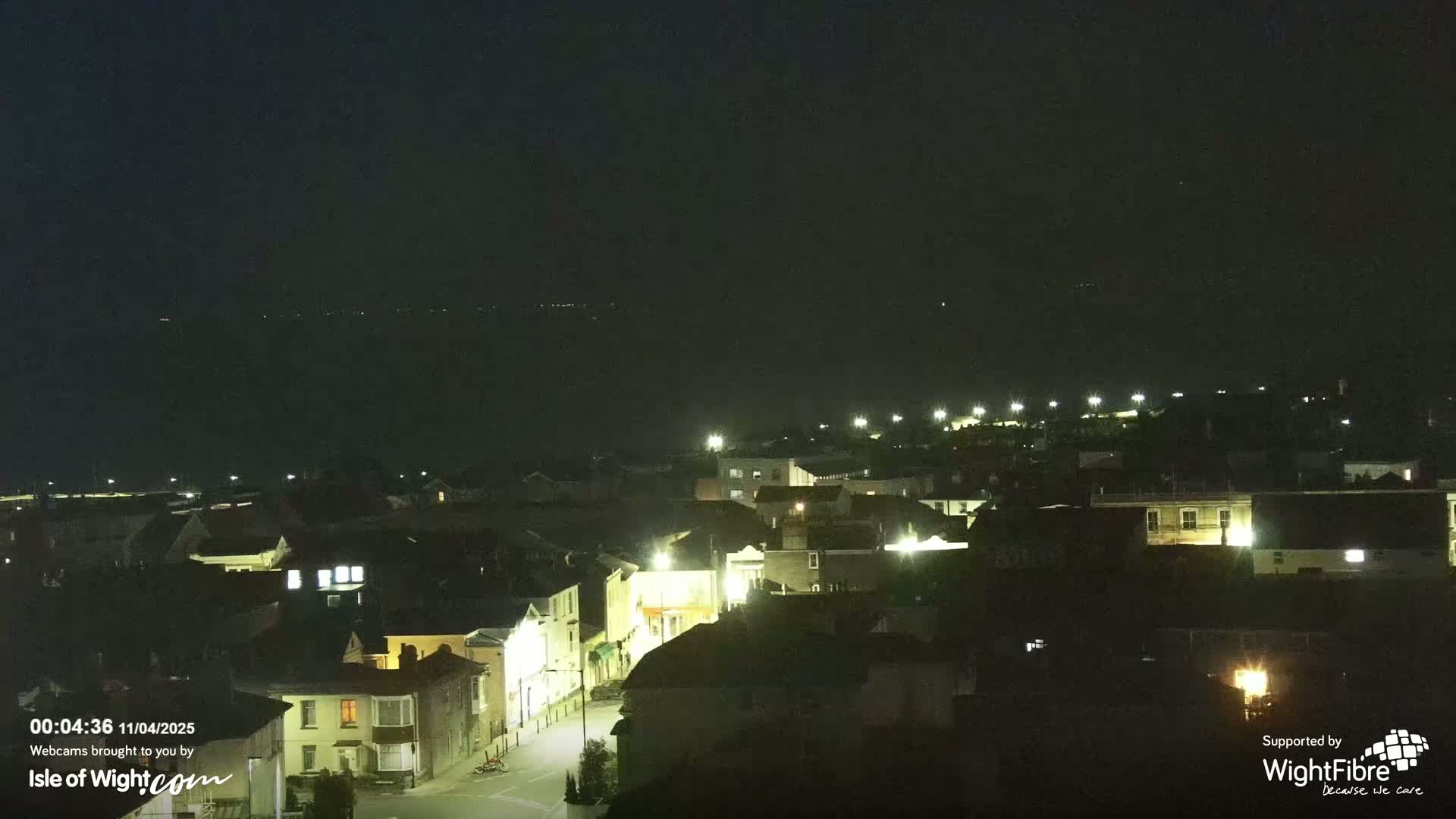 A nighttime, overhead view of a town with illuminated buildings and streets, under a dark sky.