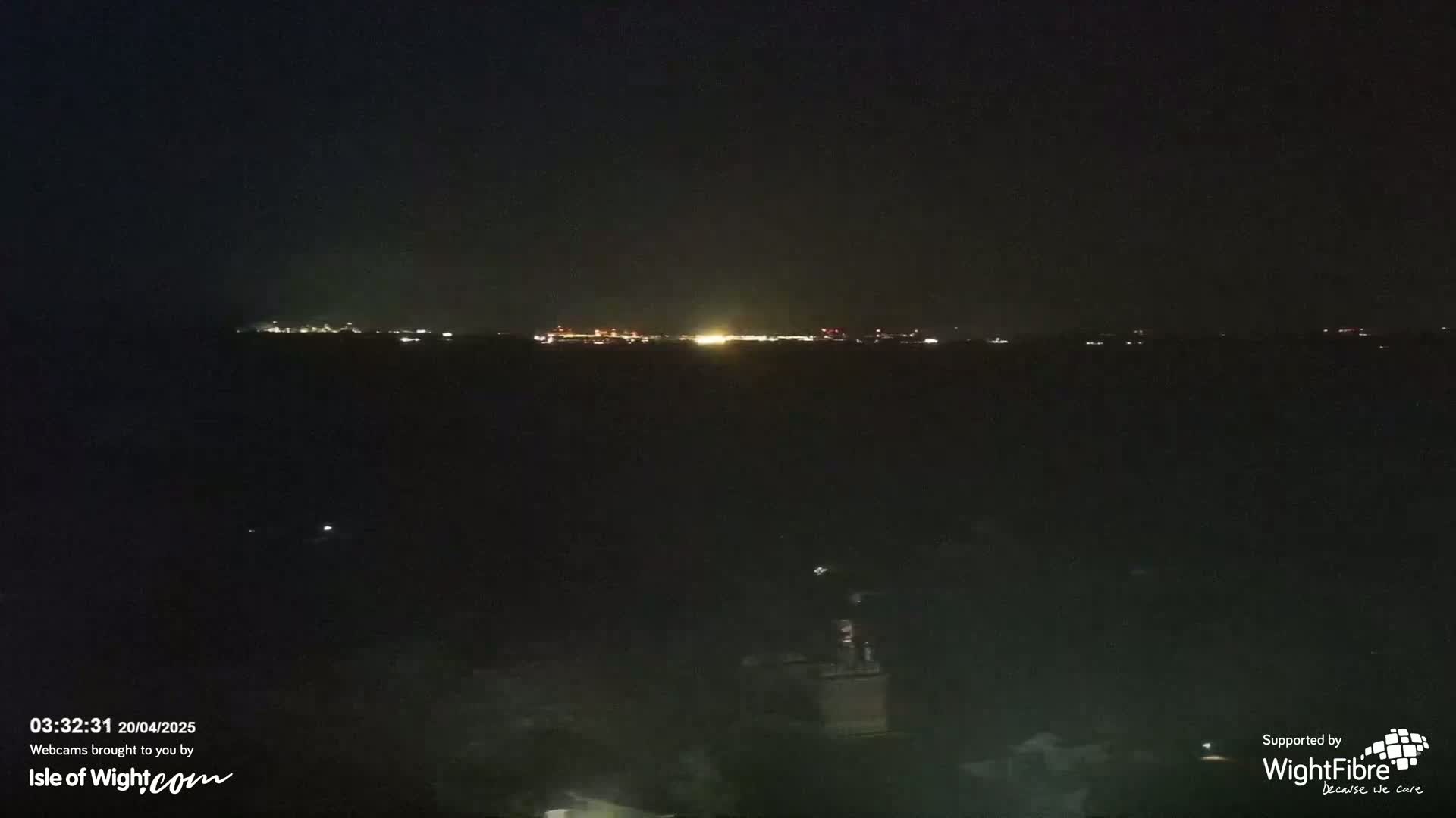 A dark, nighttime view of a body of water with a distant, faintly lit shoreline.