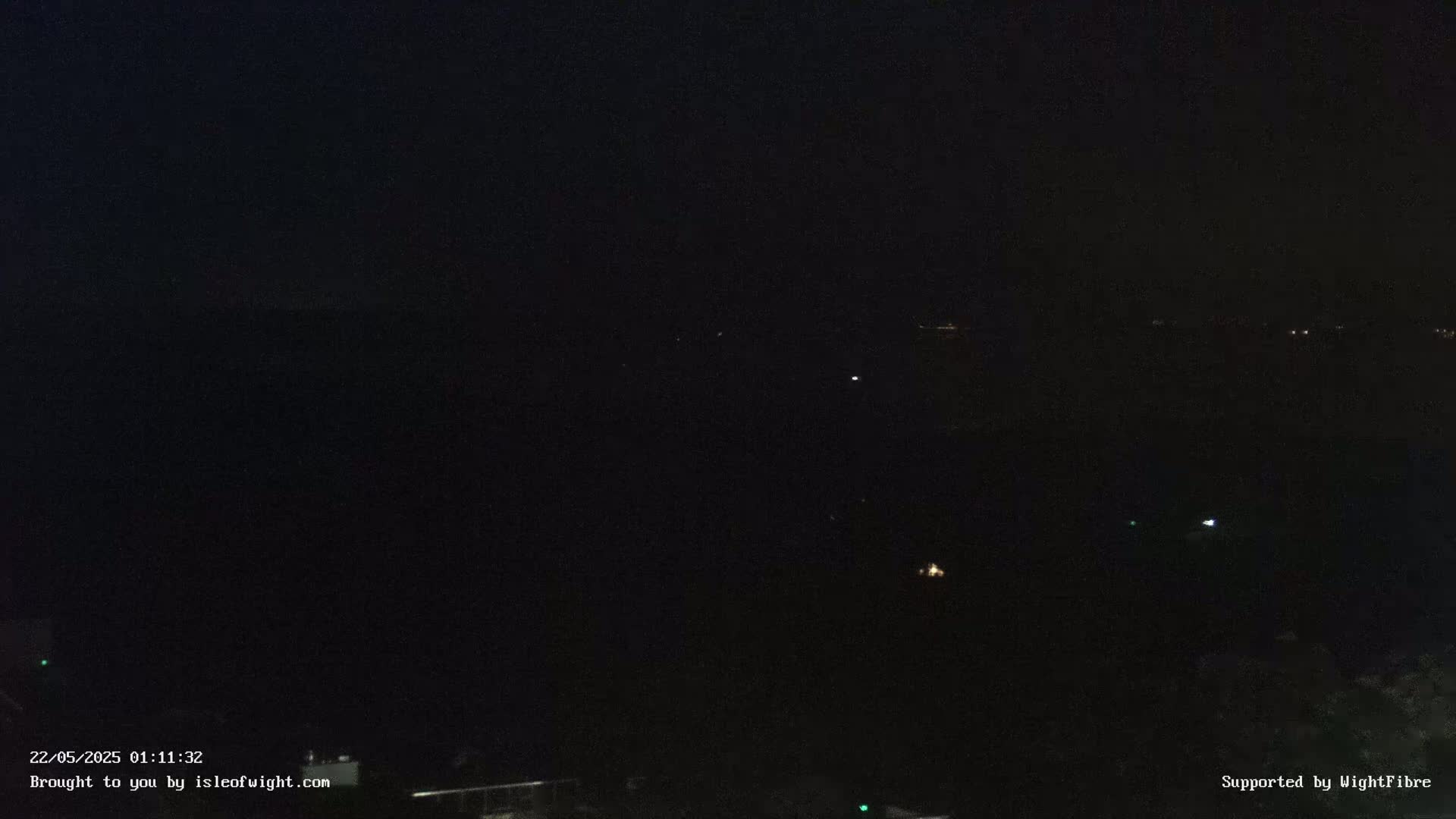 A dark nighttime scene shows a few faint lights in the distance across a black body of water.