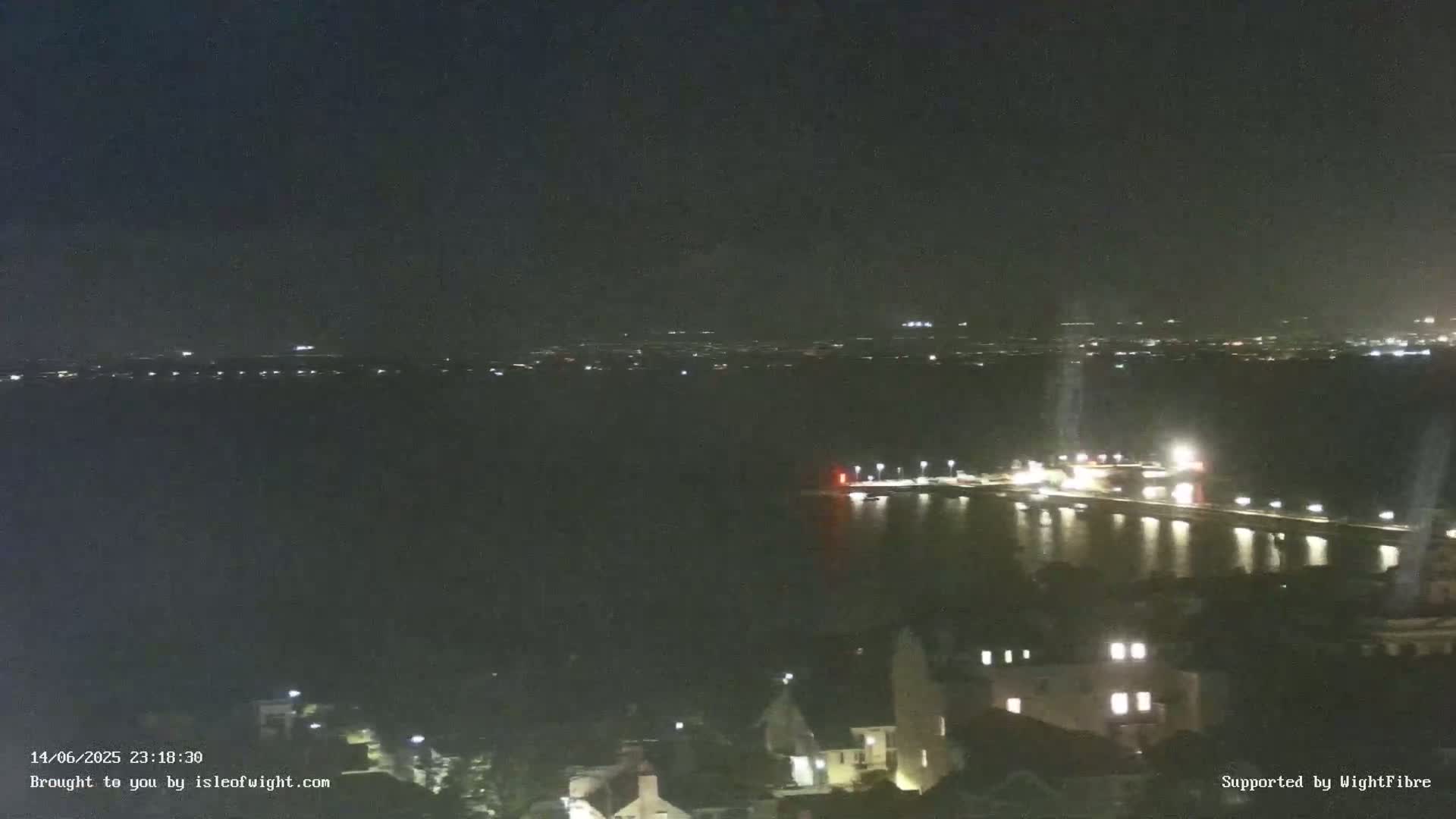 A dark nighttime scene shows a few faint lights in the distance across a black body of water.