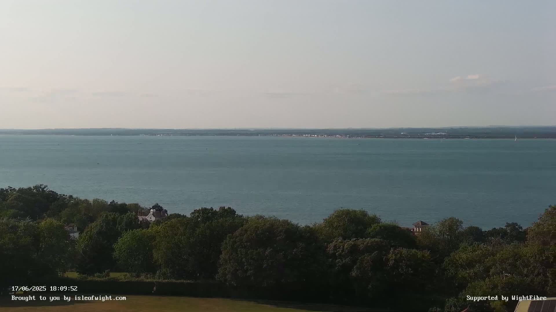 A calm, light-blue body of water stretches to a distant shoreline, partially obscured by a foreground of lush green trees.