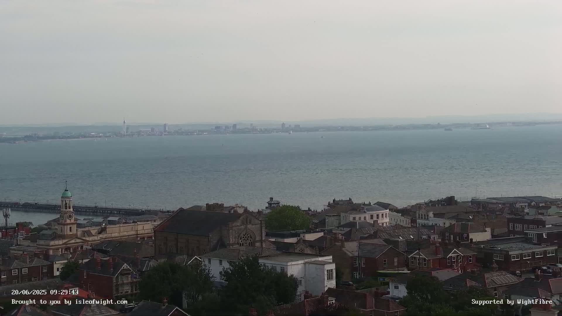A hazy view of a town and a large body of water, with a distant cityscape on the horizon.